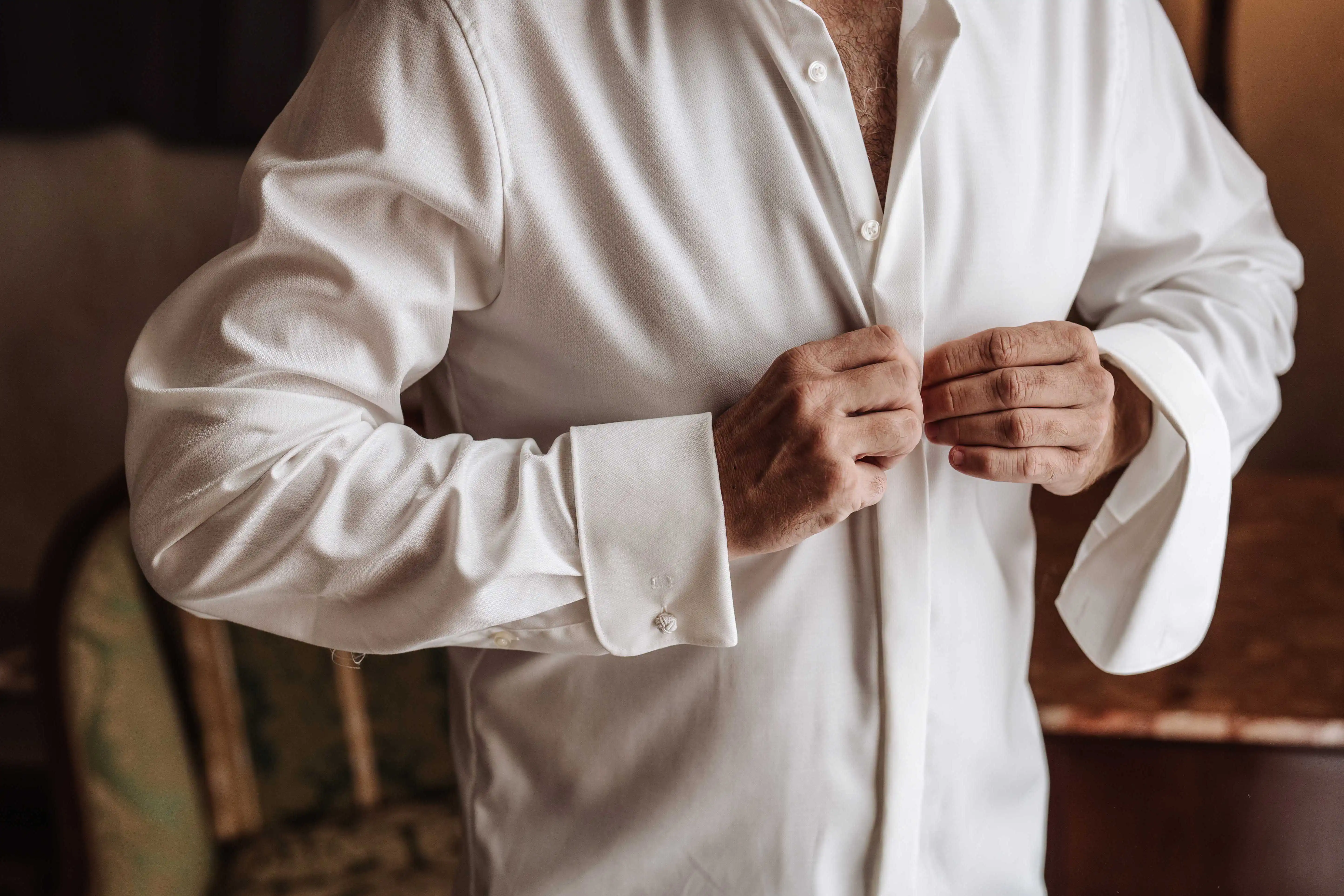groom buttoning white shirt close up wedding morning details