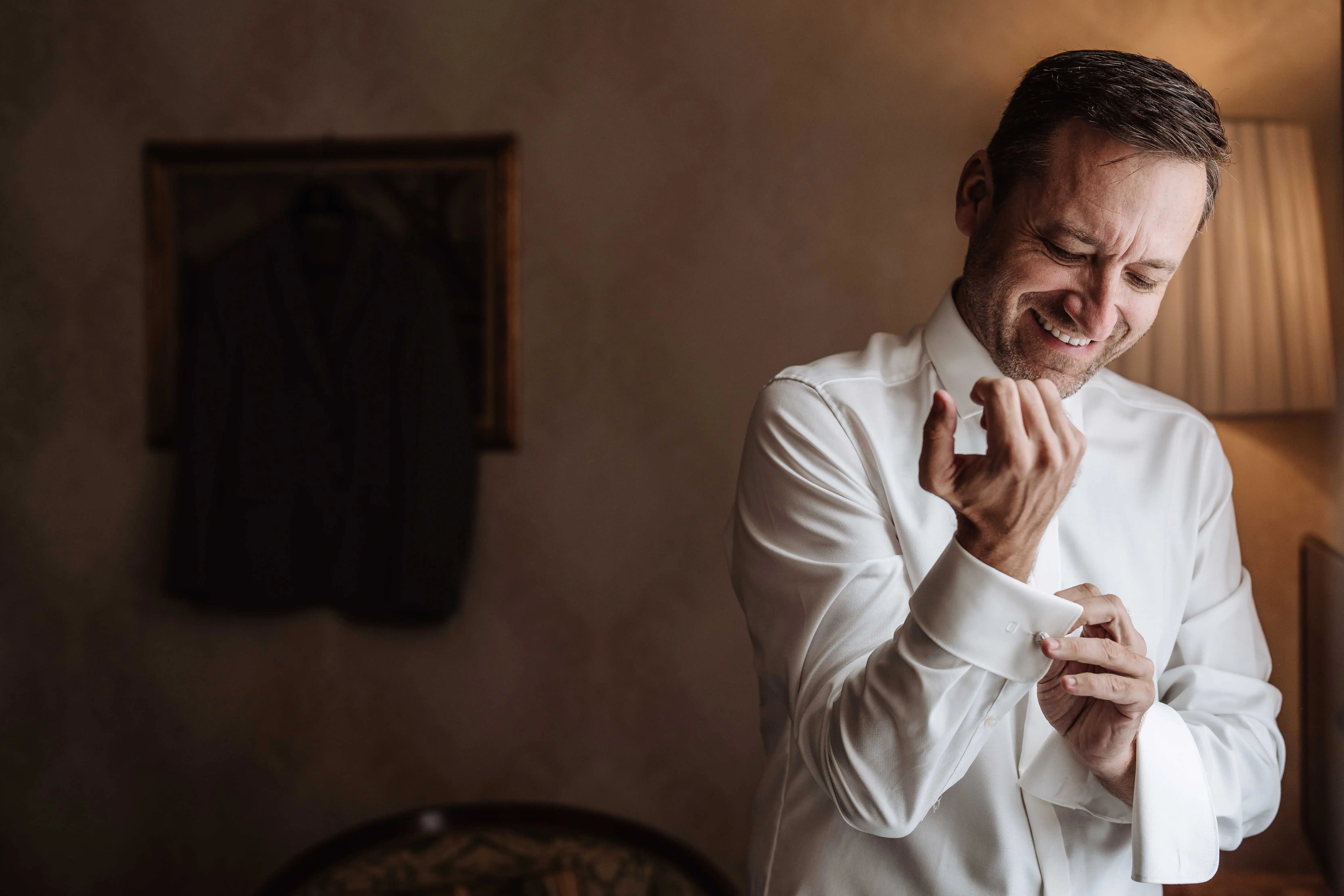 groom putting on cufflinks smiling candid wedding preparation