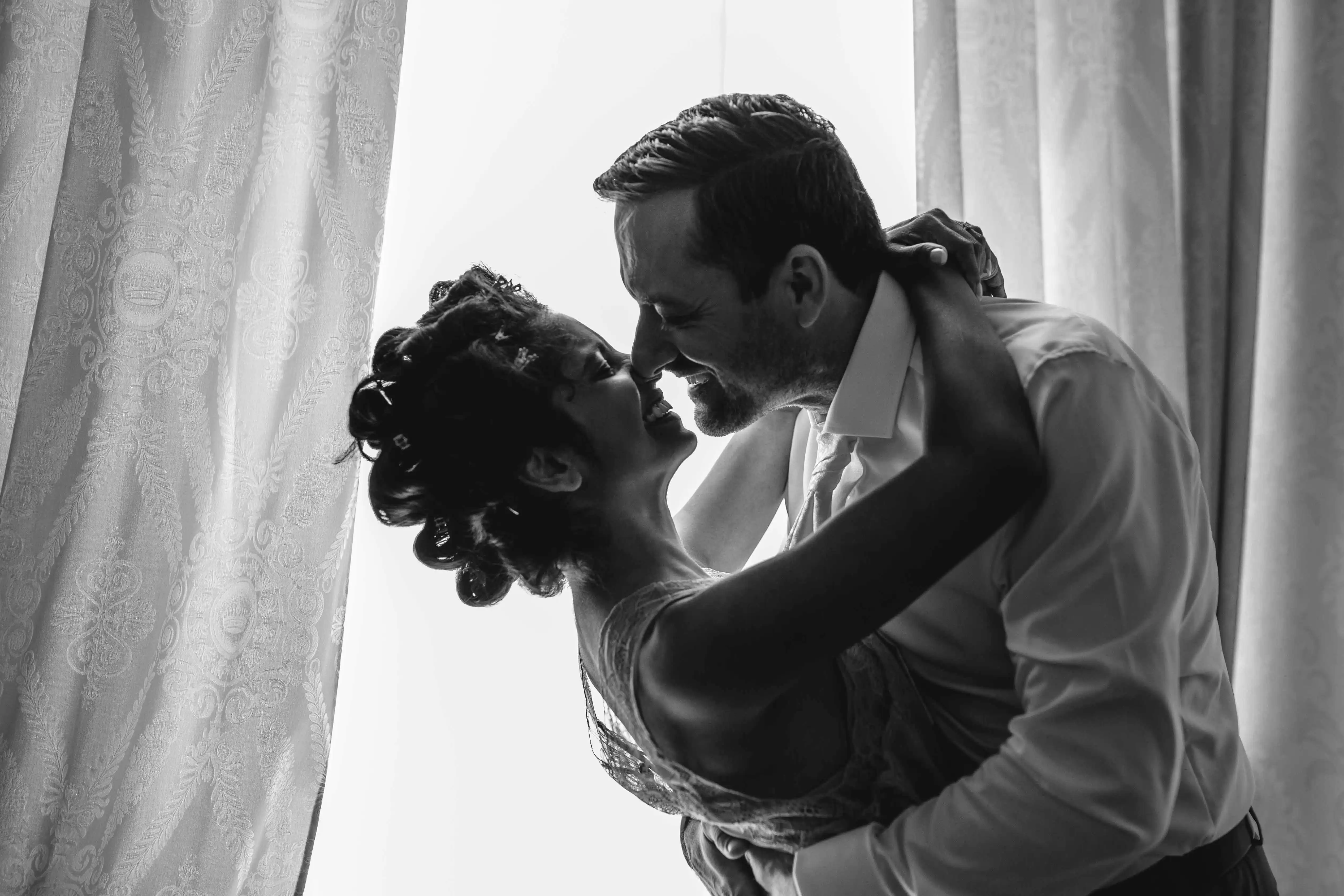 Bride and groom smiling in soft backlight sharing an intimate moment before the ceremony