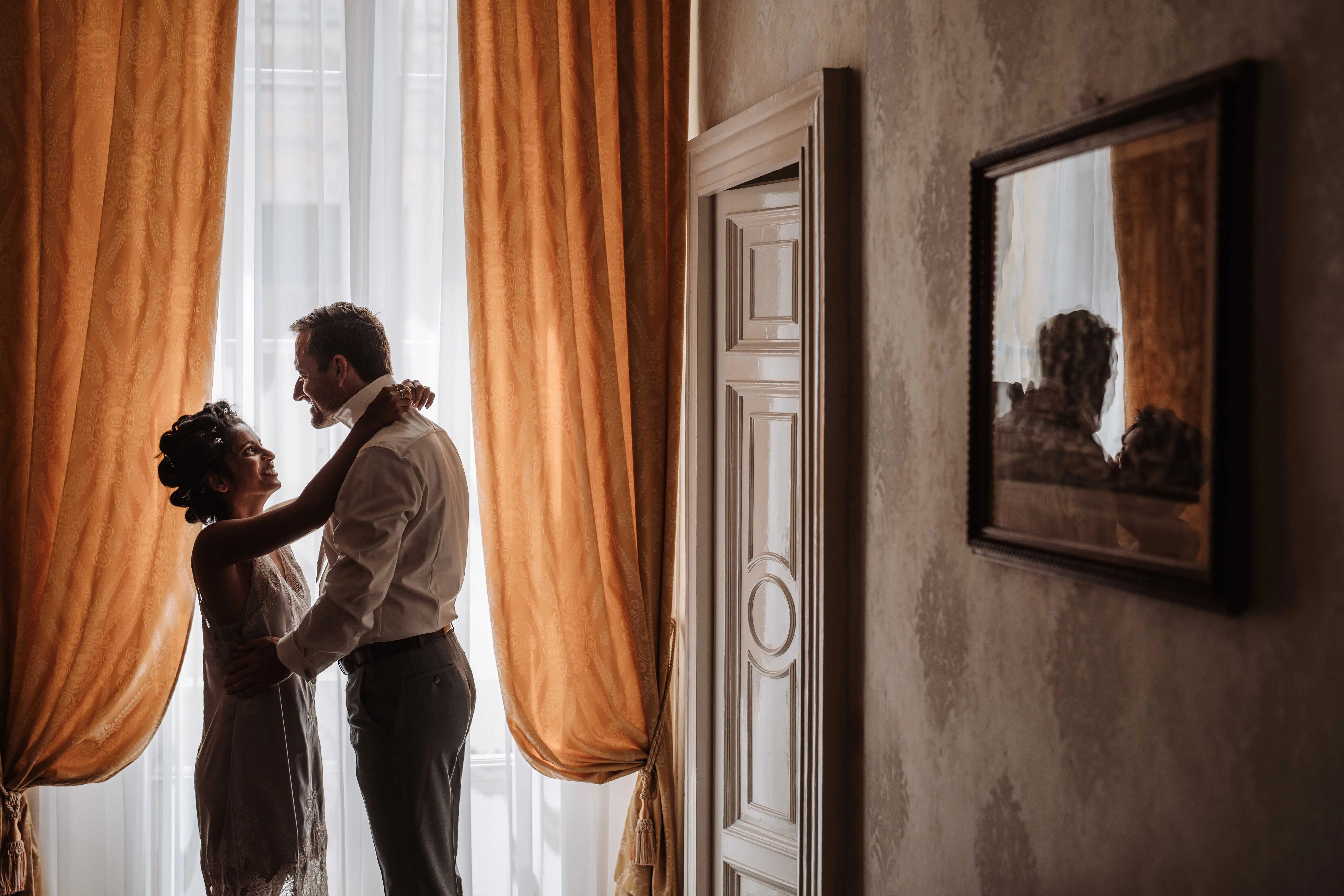 Bride embracing groom near a window with elegant curtains in a bright room