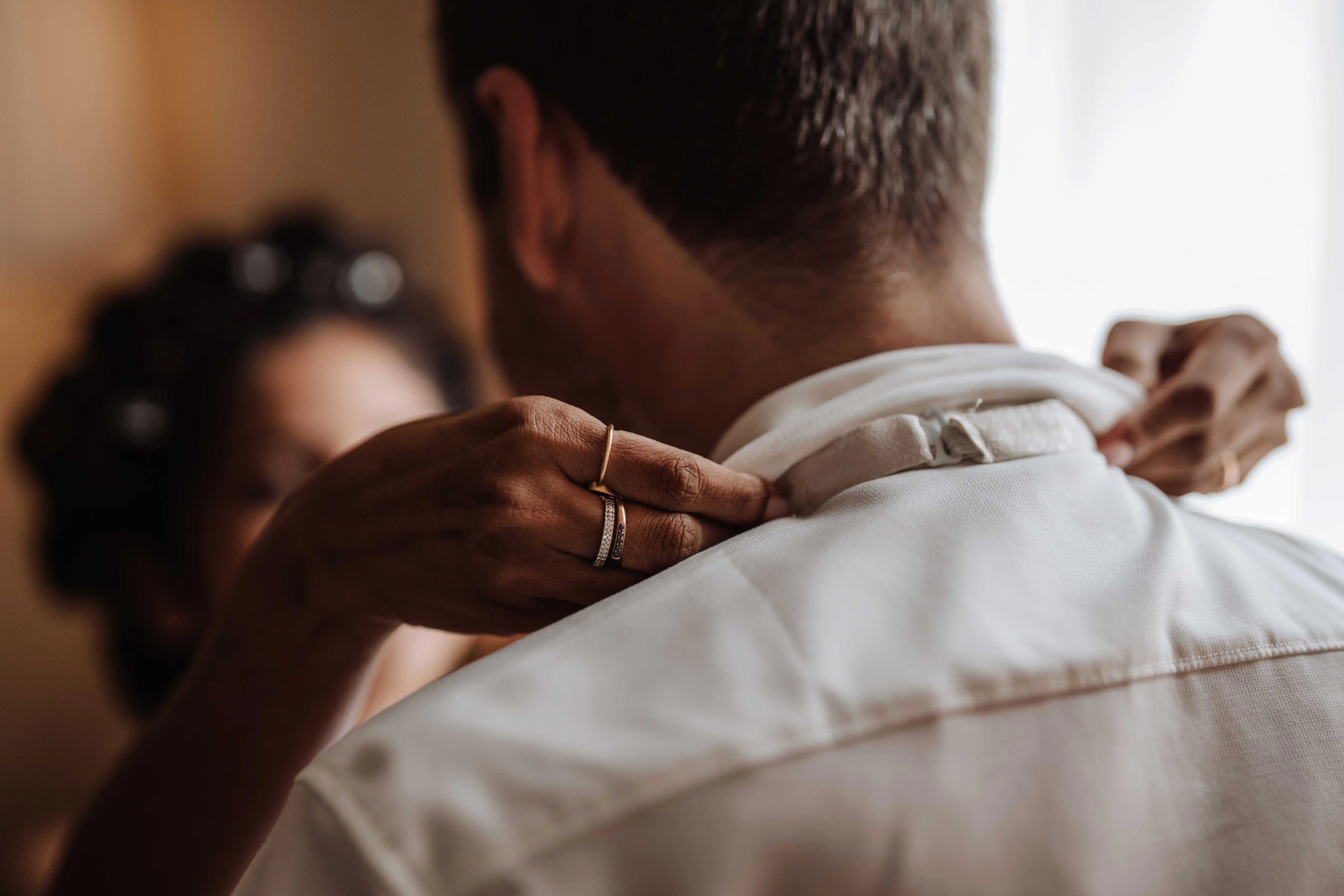 Close-up of bride adjusting groom’s shirt collar during getting ready