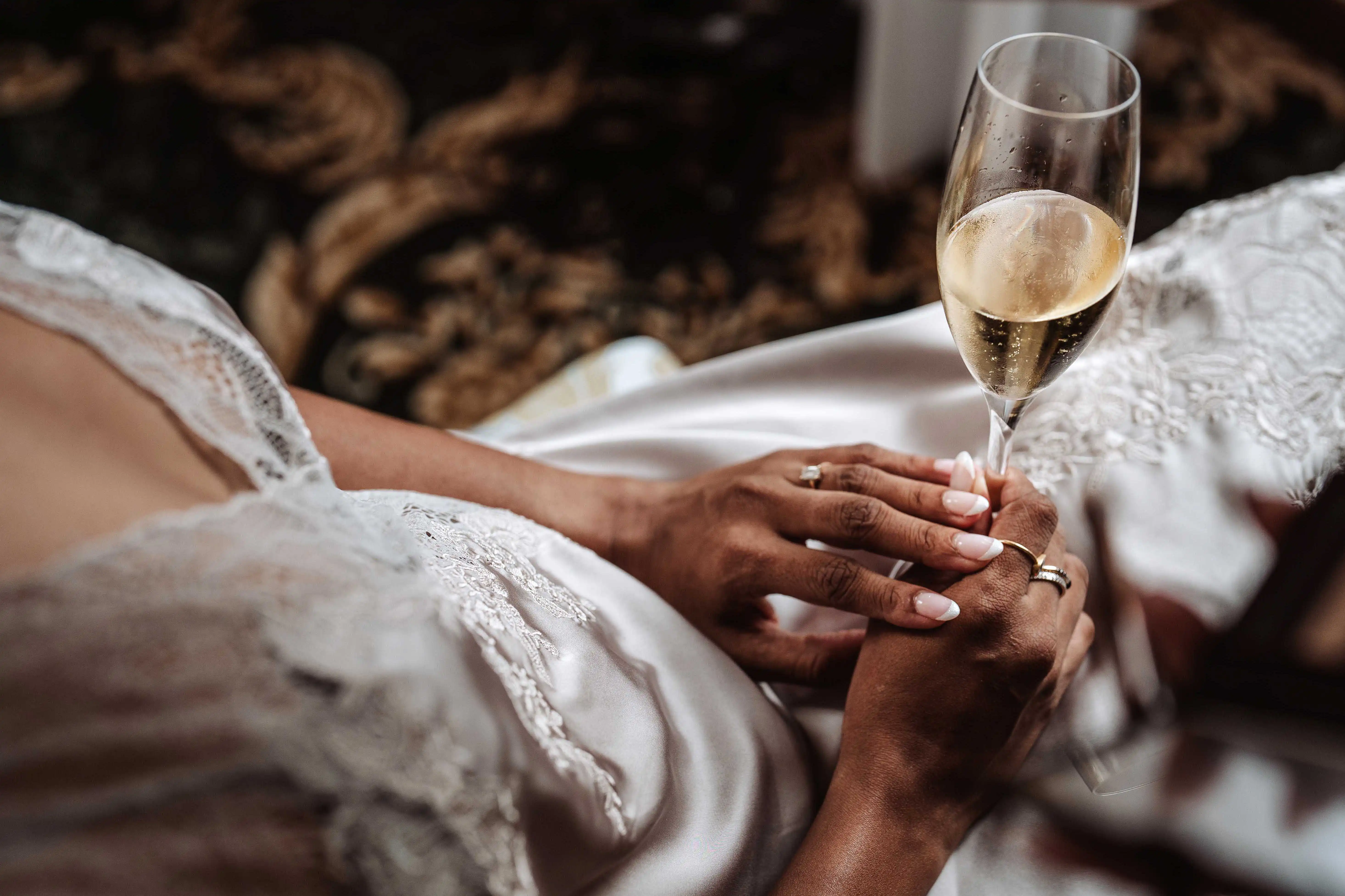 Close-up of bride’s hands holding champagne glass with engagement ring detail