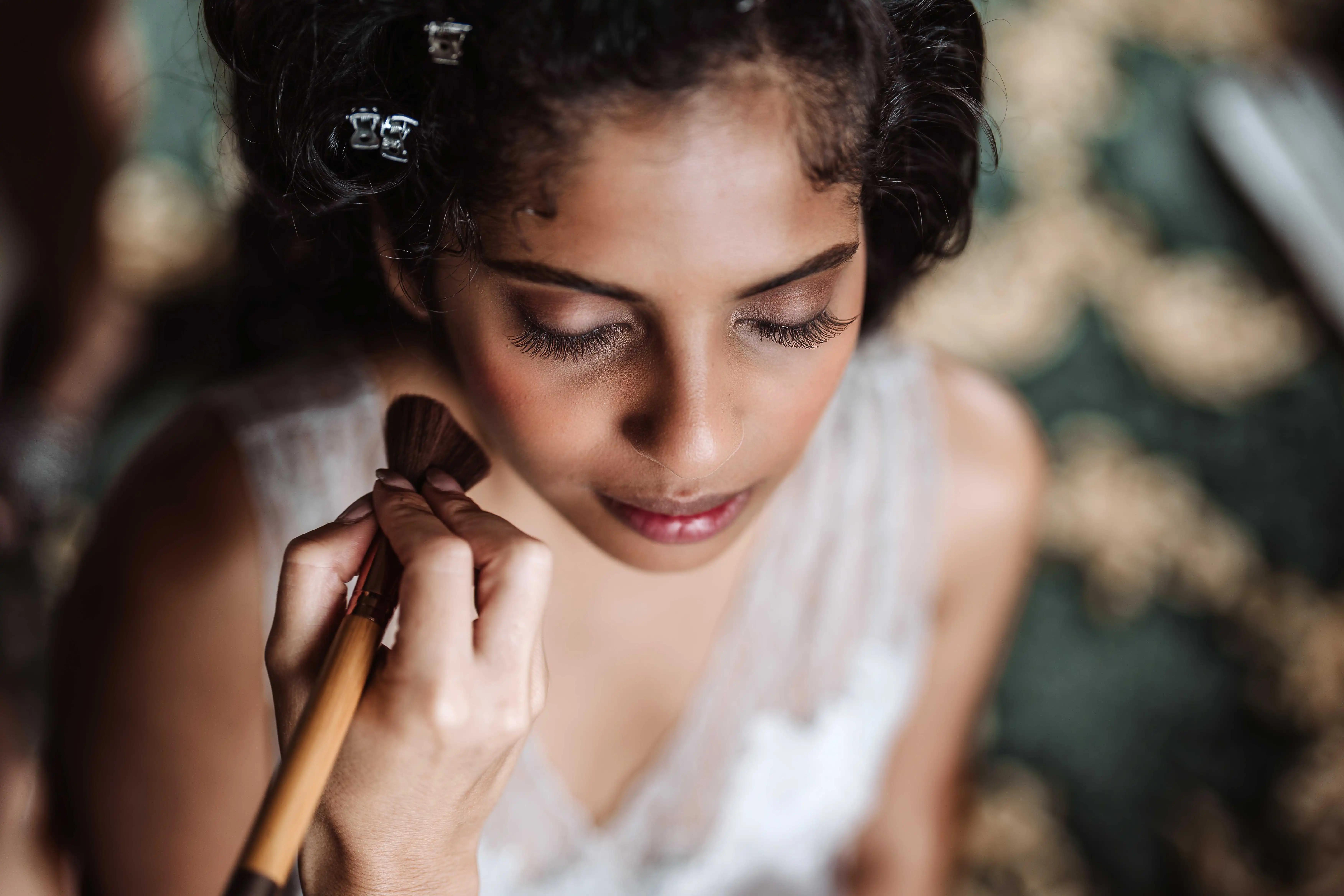 Bride having makeup applied with soft natural light during wedding morning