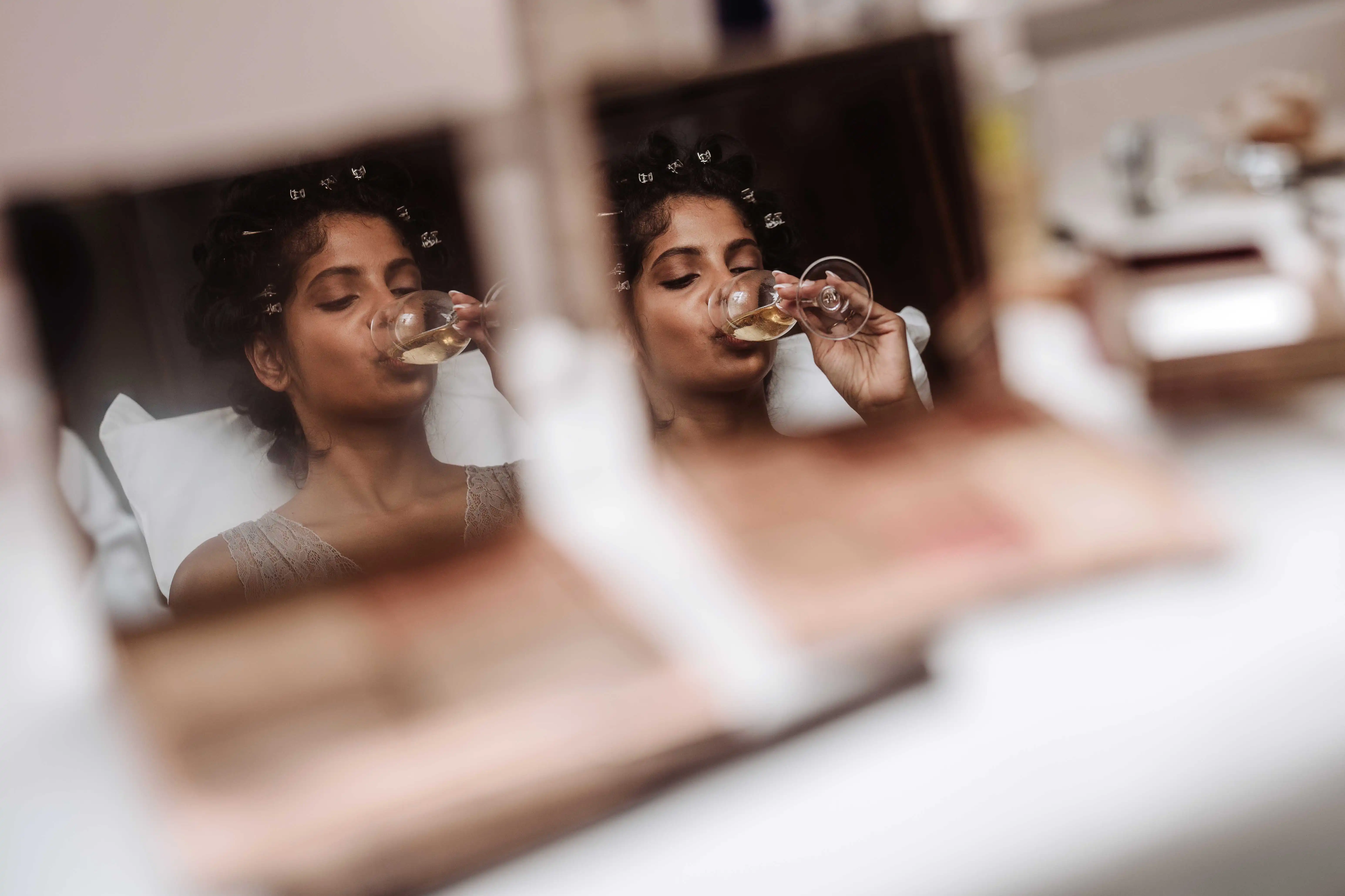 Creative reflection of bride drinking champagne seen through mirror