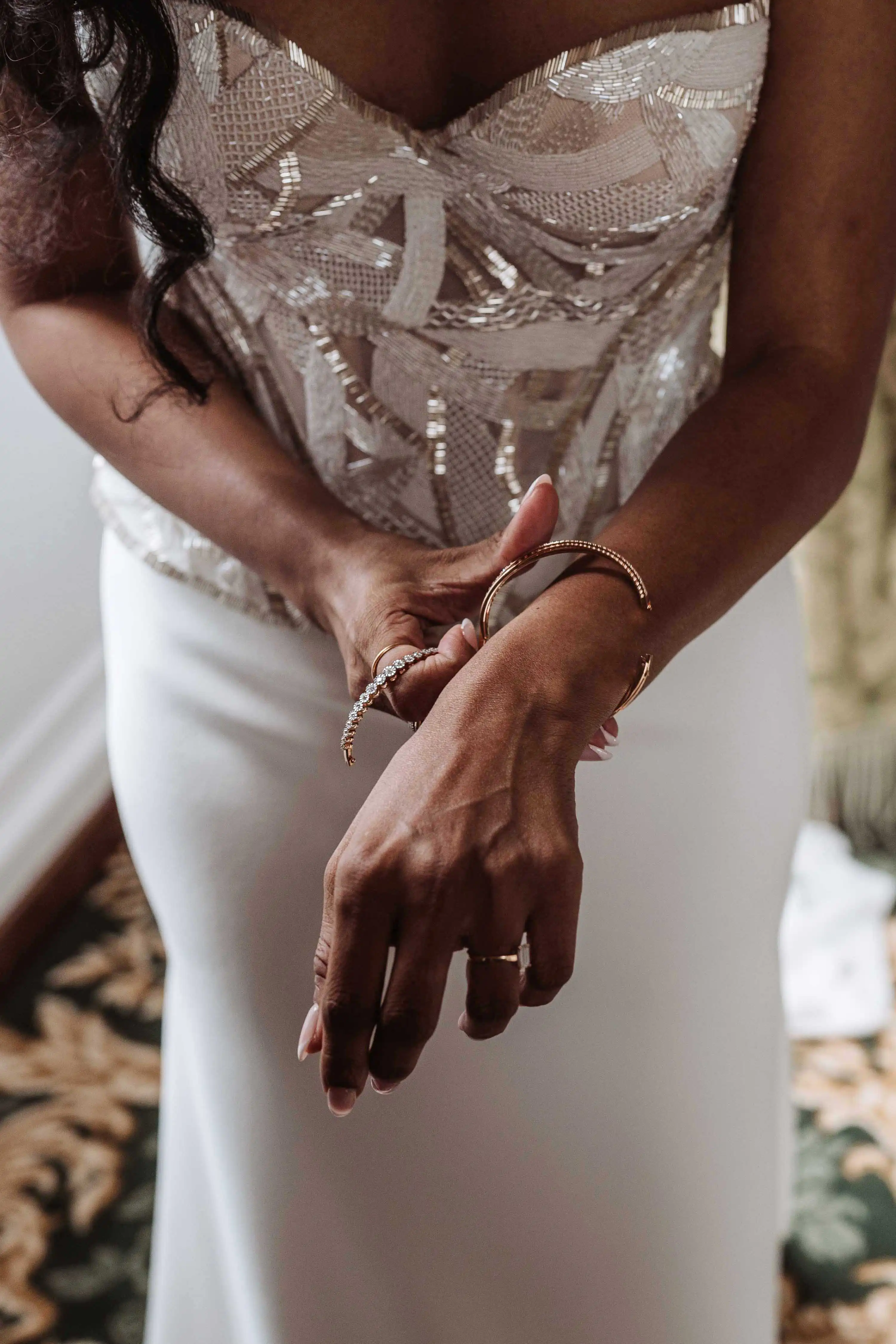 Close-up of bride adjusting bracelet with detailed beaded wedding bodice
