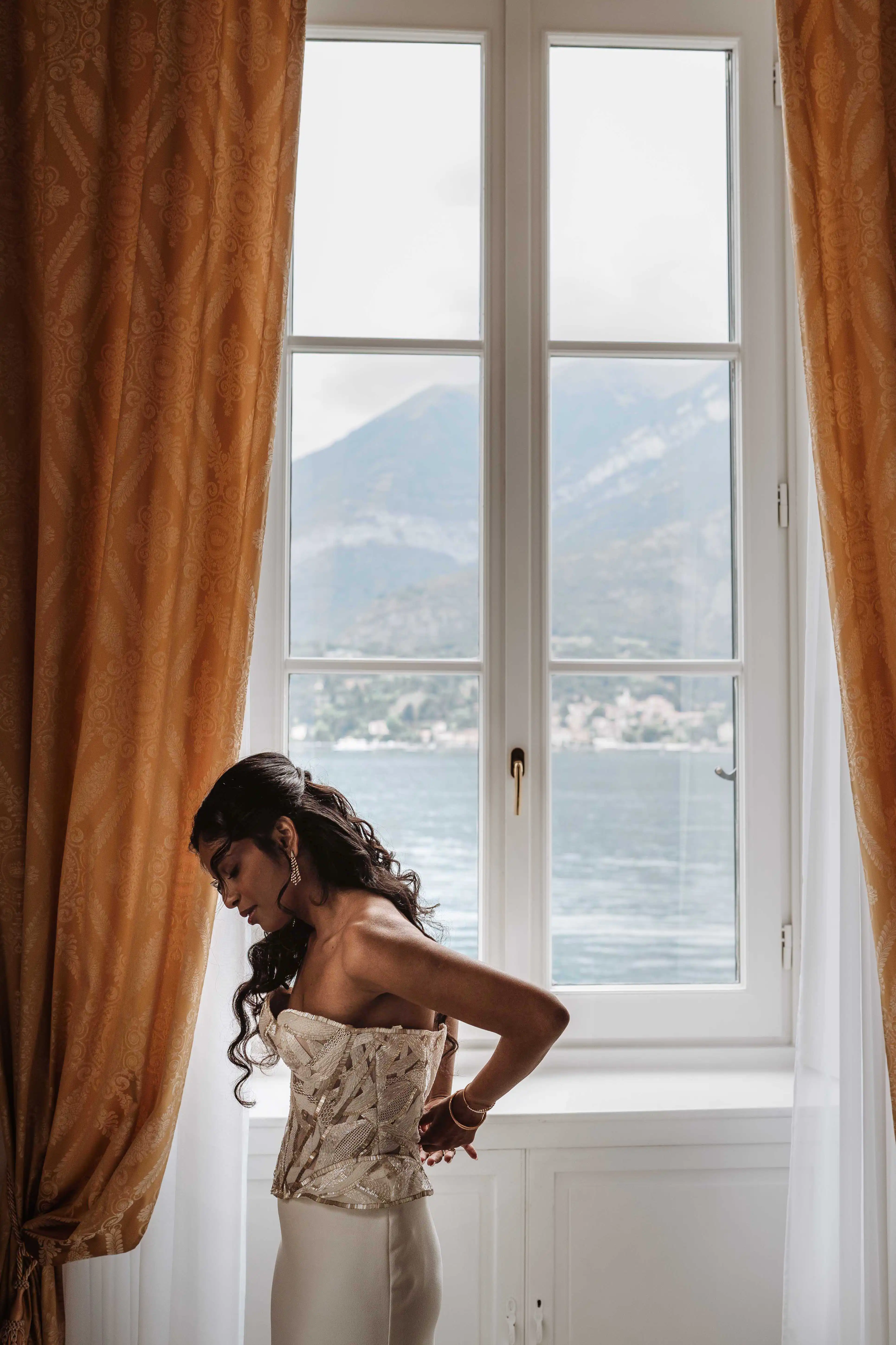 Bride getting dressed by window with Lake Como view and soft natural light