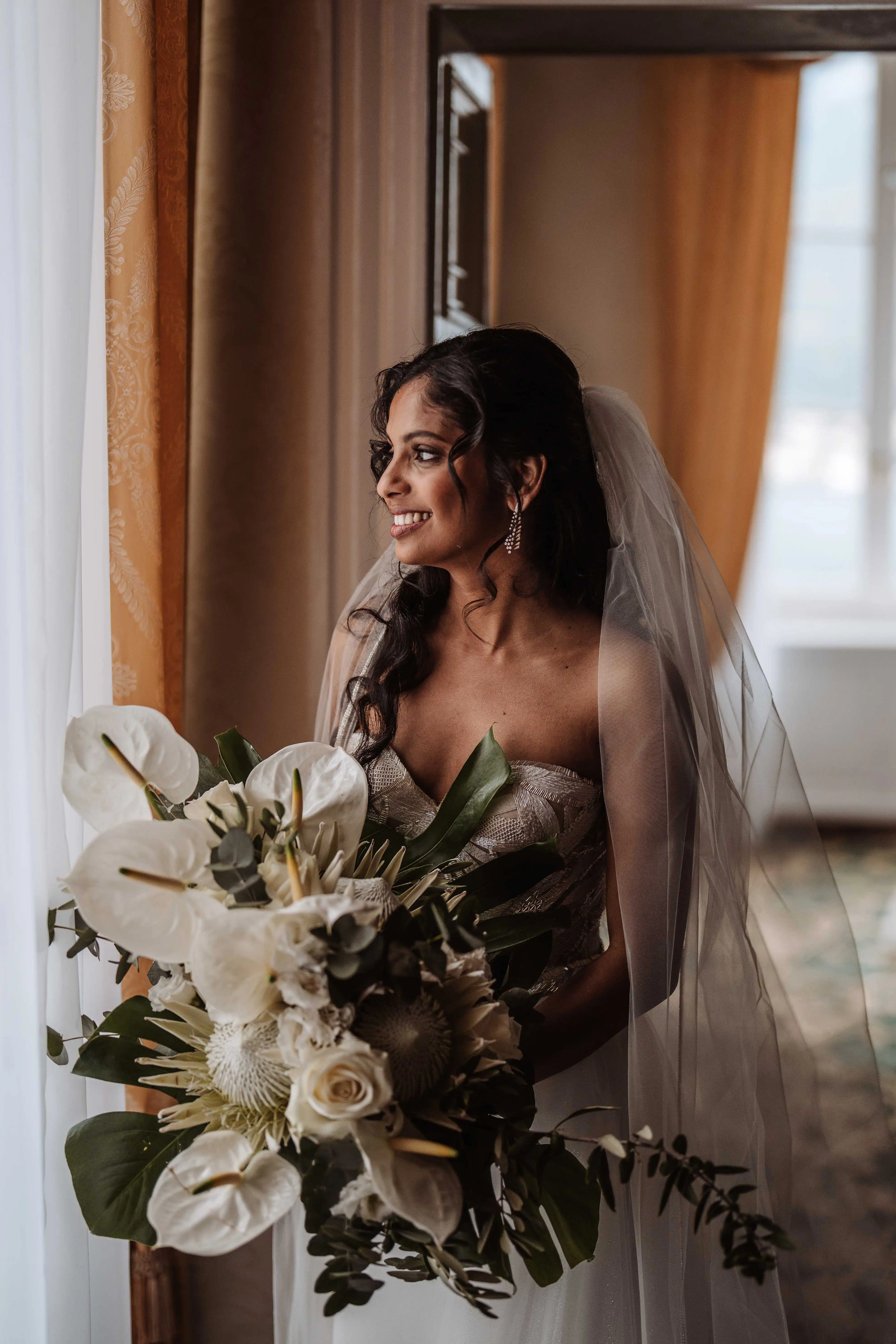 Bride with veil holding bouquet by window in Lake Como wedding morning