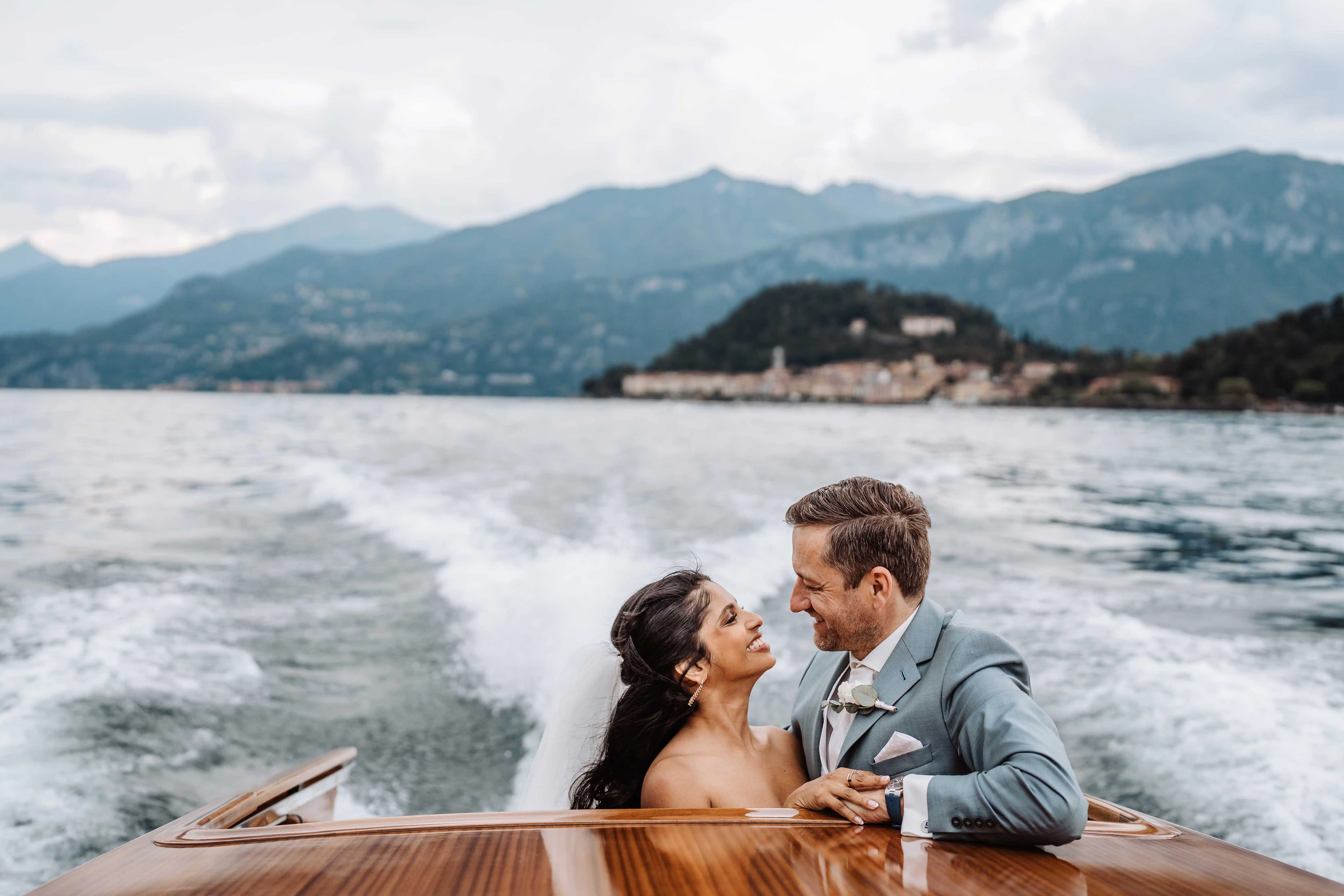 Newlyweds embracing on boat with Lake Como mountains in background