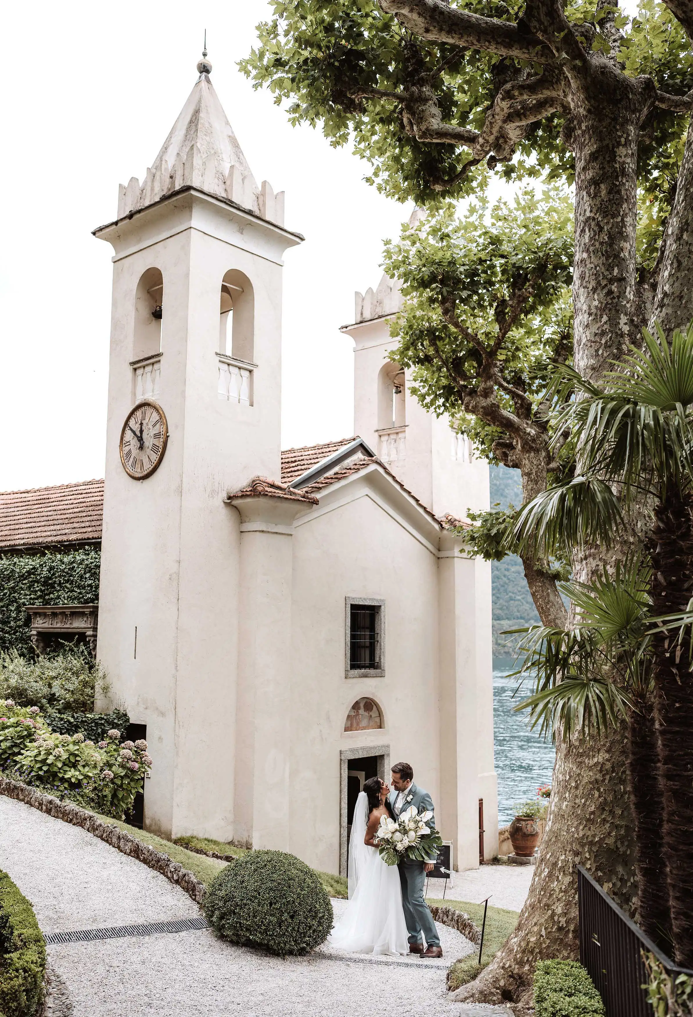 Romantic couple standing by a small historic church tower overlooking Lake Como