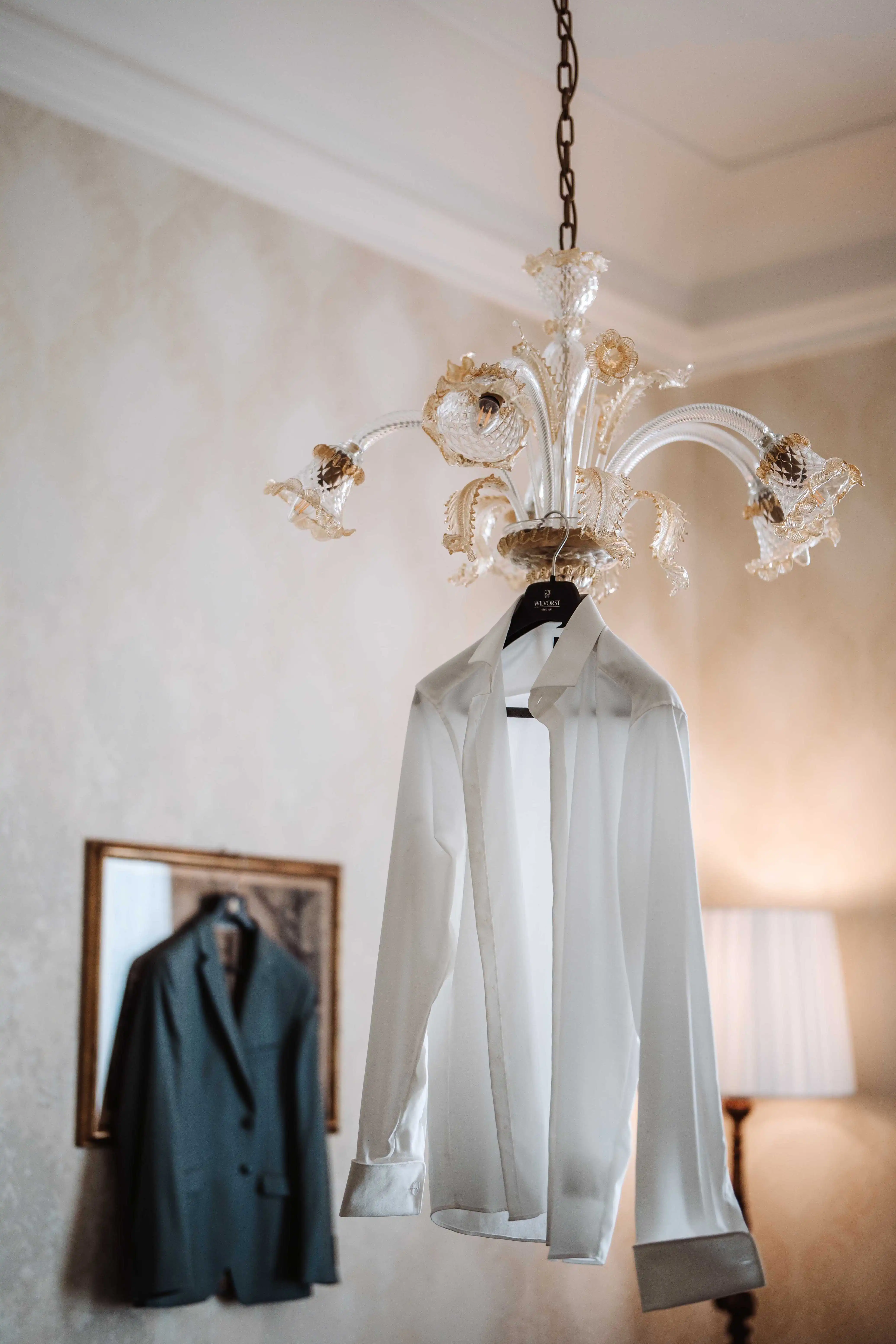 Refined groom shirt hanging under chandelier in luxury wedding venue in Italy