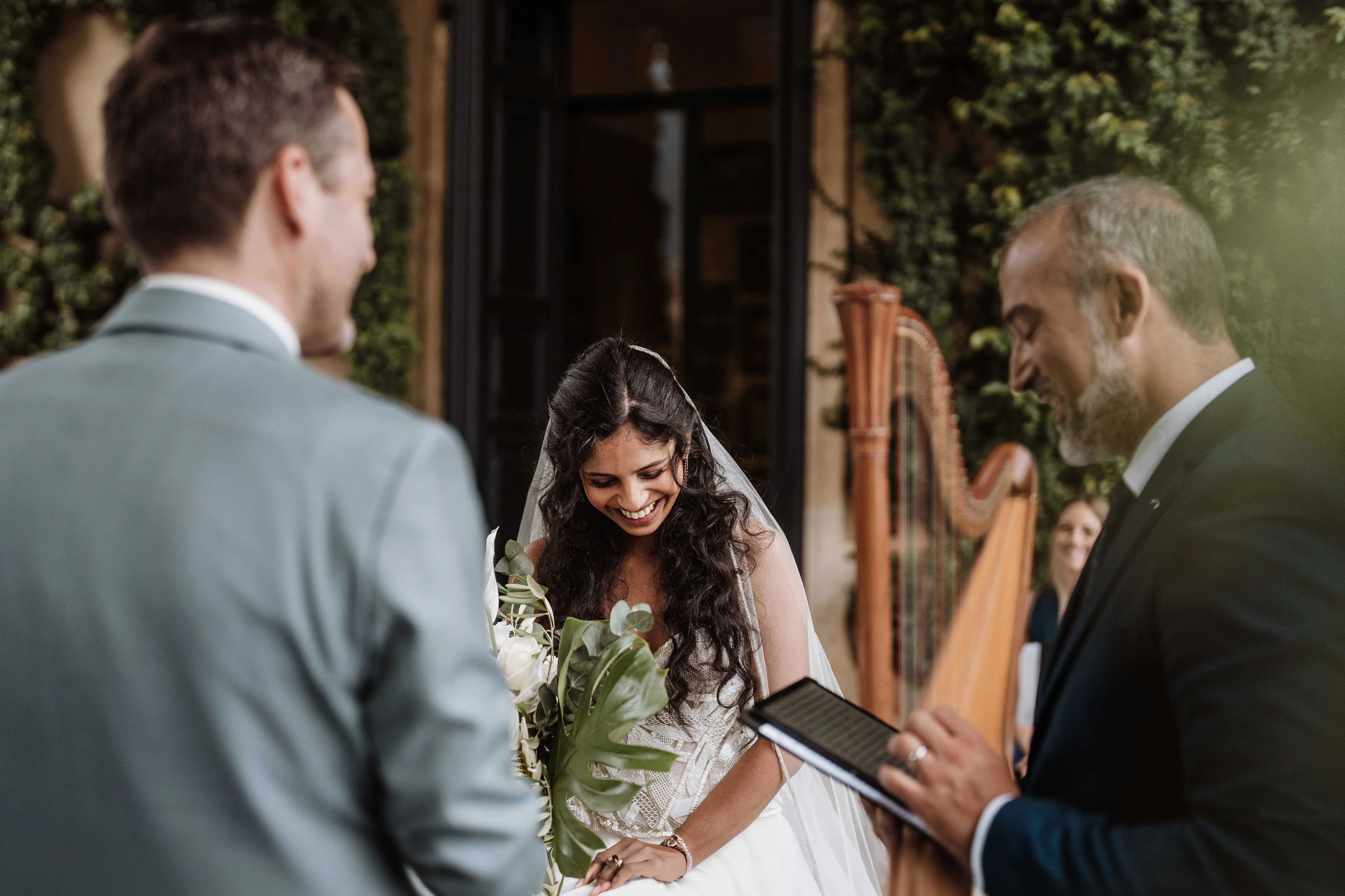 Emotional moment during the wedding ceremony as bride smiles holding bouquet while officiant reads vows