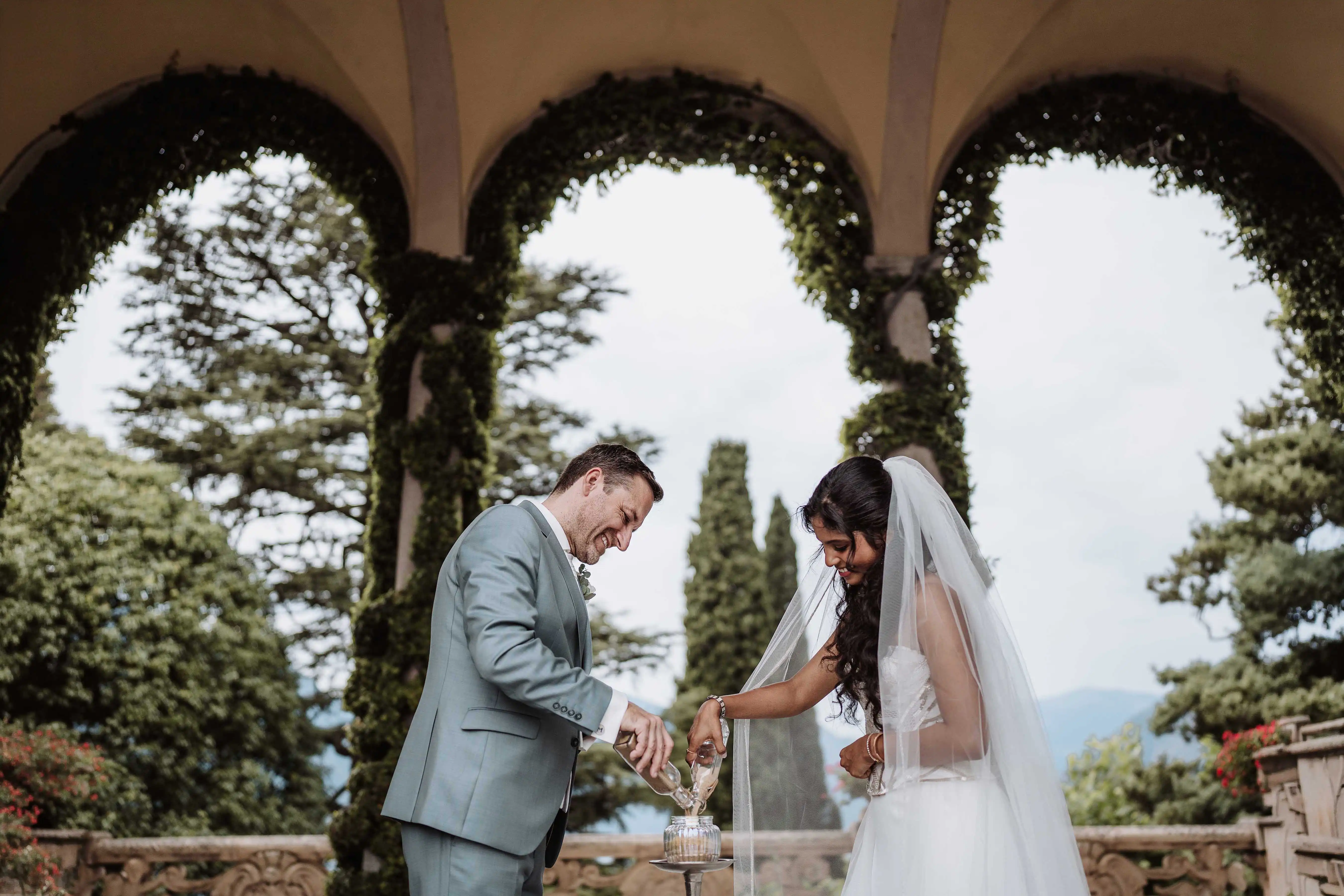 Couple performing a symbolic ritual together under a garden arch at their Lake Como wedding