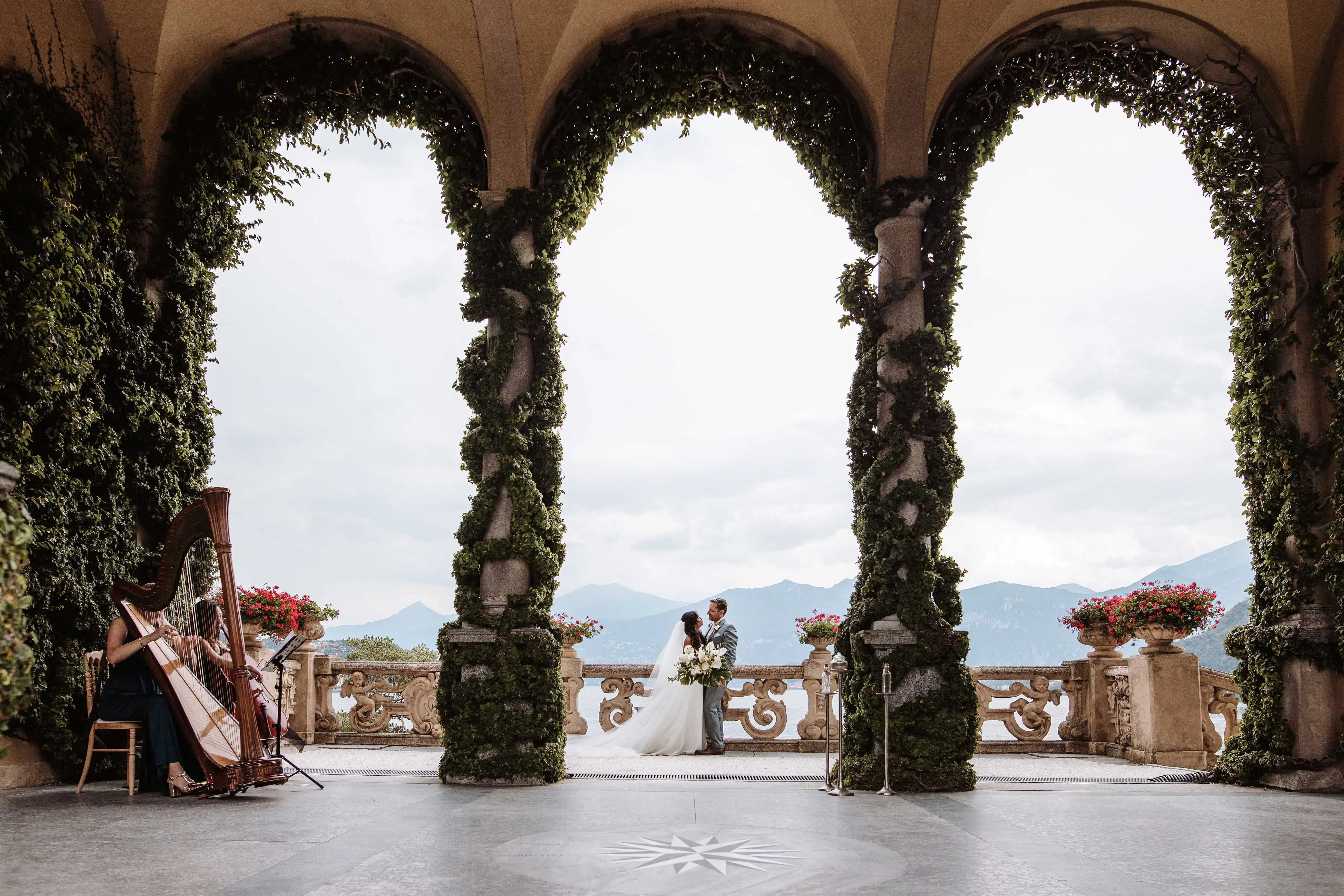 Wide view of a Lake Como wedding ceremony on a panoramic terrace with ivy-covered arches and lake view