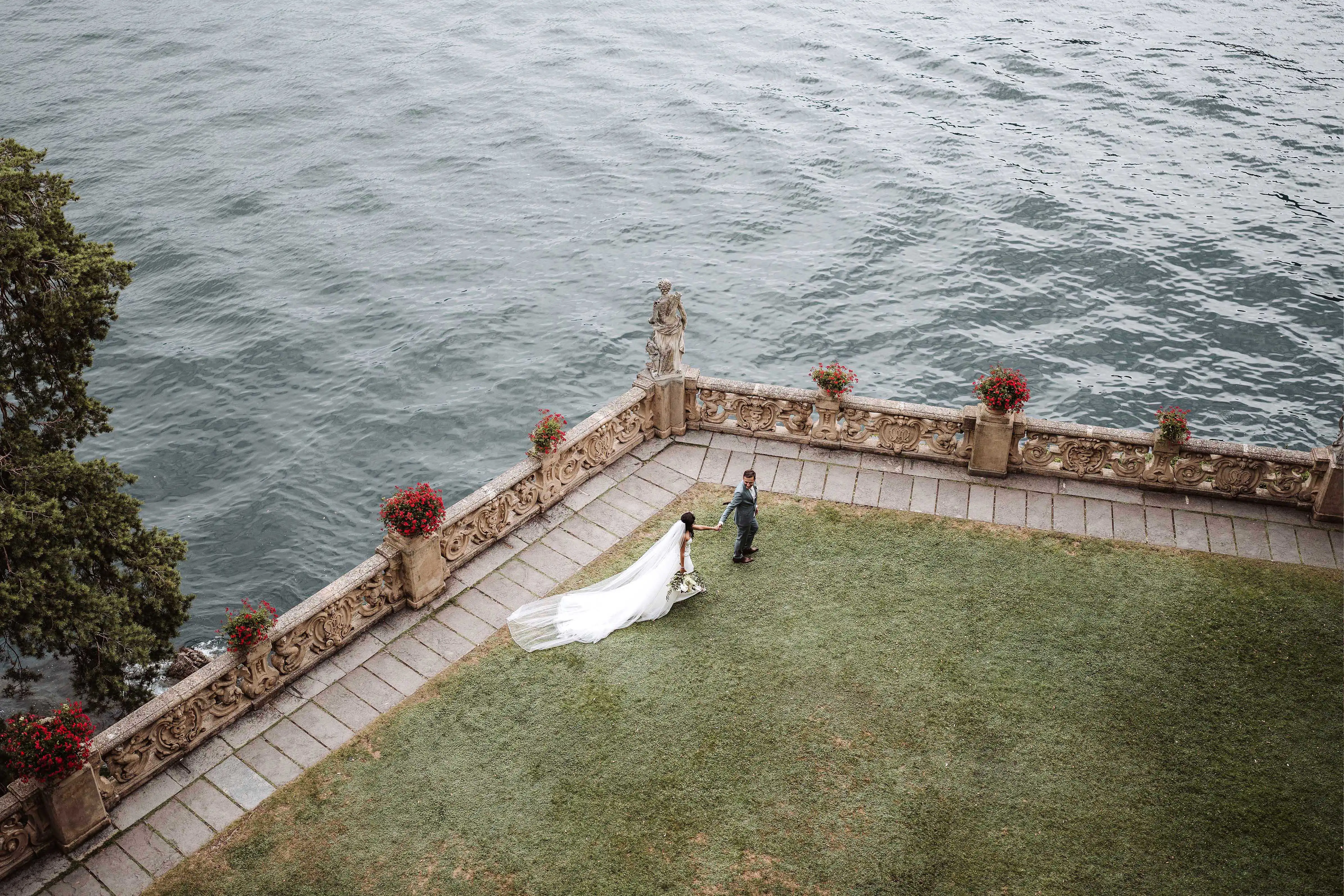 Aerial view of bride and groom on a terrace by Lake Como with long veil and refined architectural setting