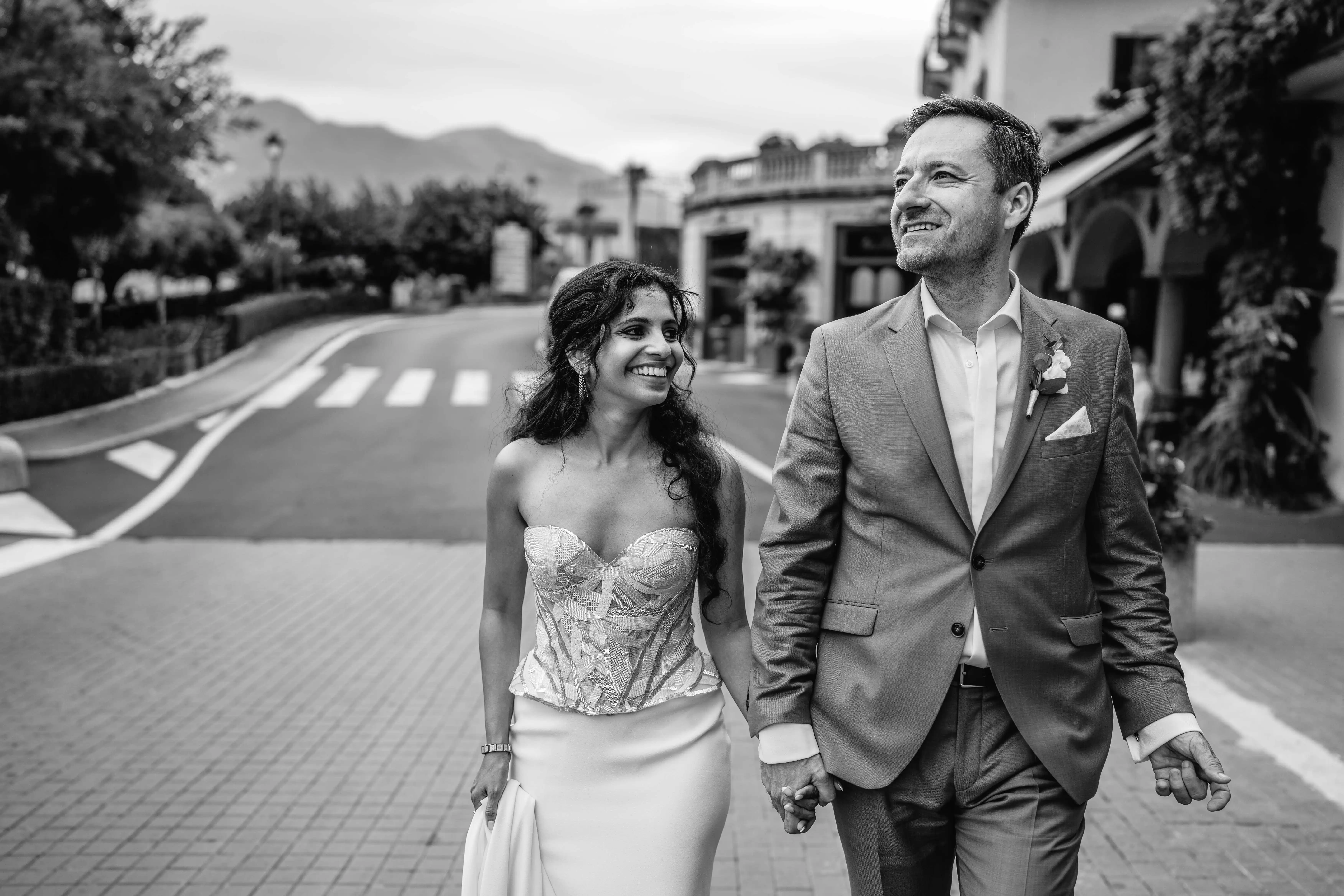Stylish couple walking hand in hand through a charming Lake Como village street in a candid black and white wedding portrait