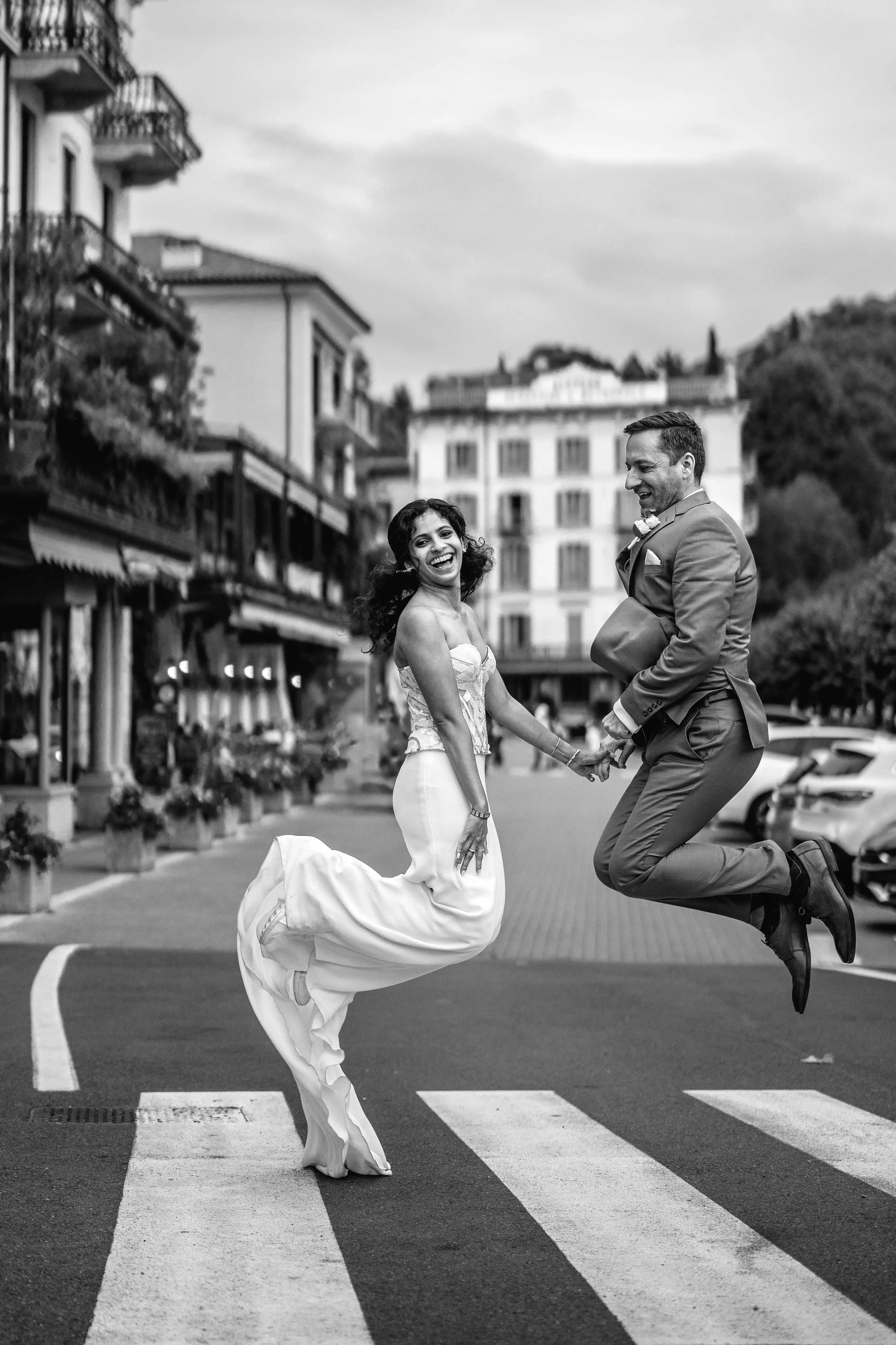 Joyful bride and groom jumping together on a crosswalk during a fun and spontaneous Lake Como wedding photo session