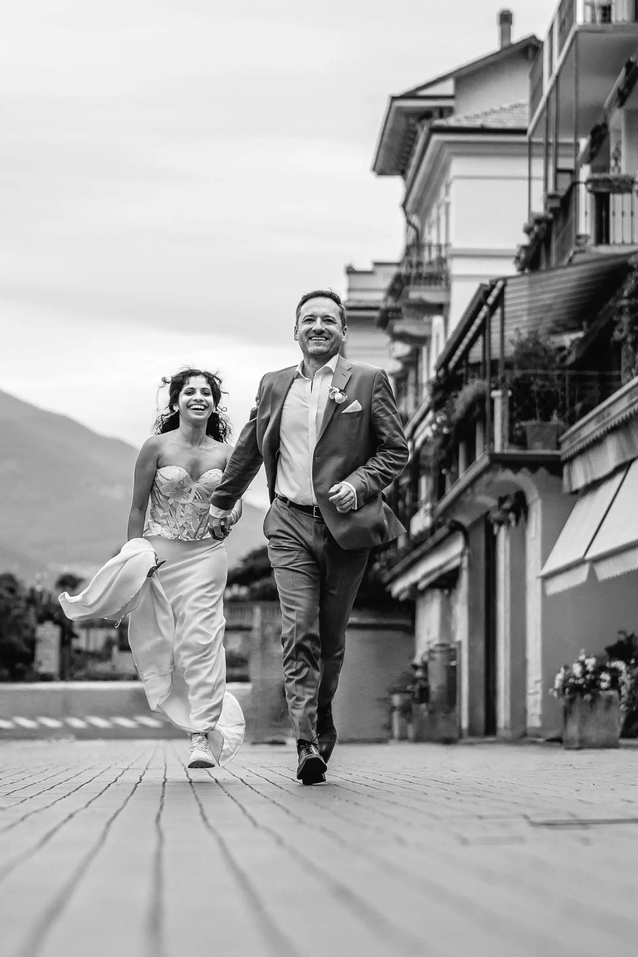 Bride and groom running together through a picturesque Lake Como street in a dynamic black and white wedding portrait