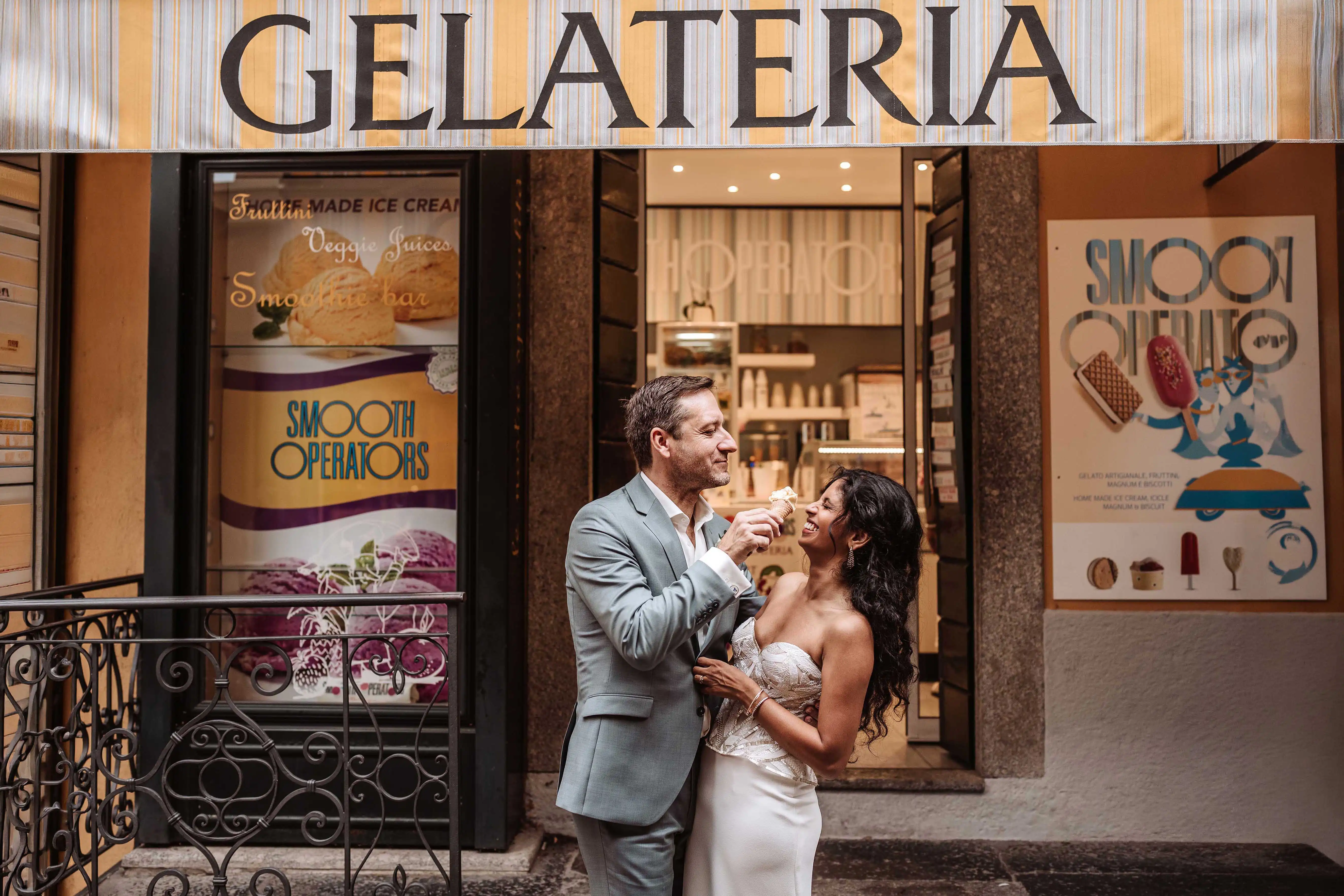 Bride and groom laughing together while eating ice cream in front of a gelateria in Lake Como, capturing a candid wedding moment