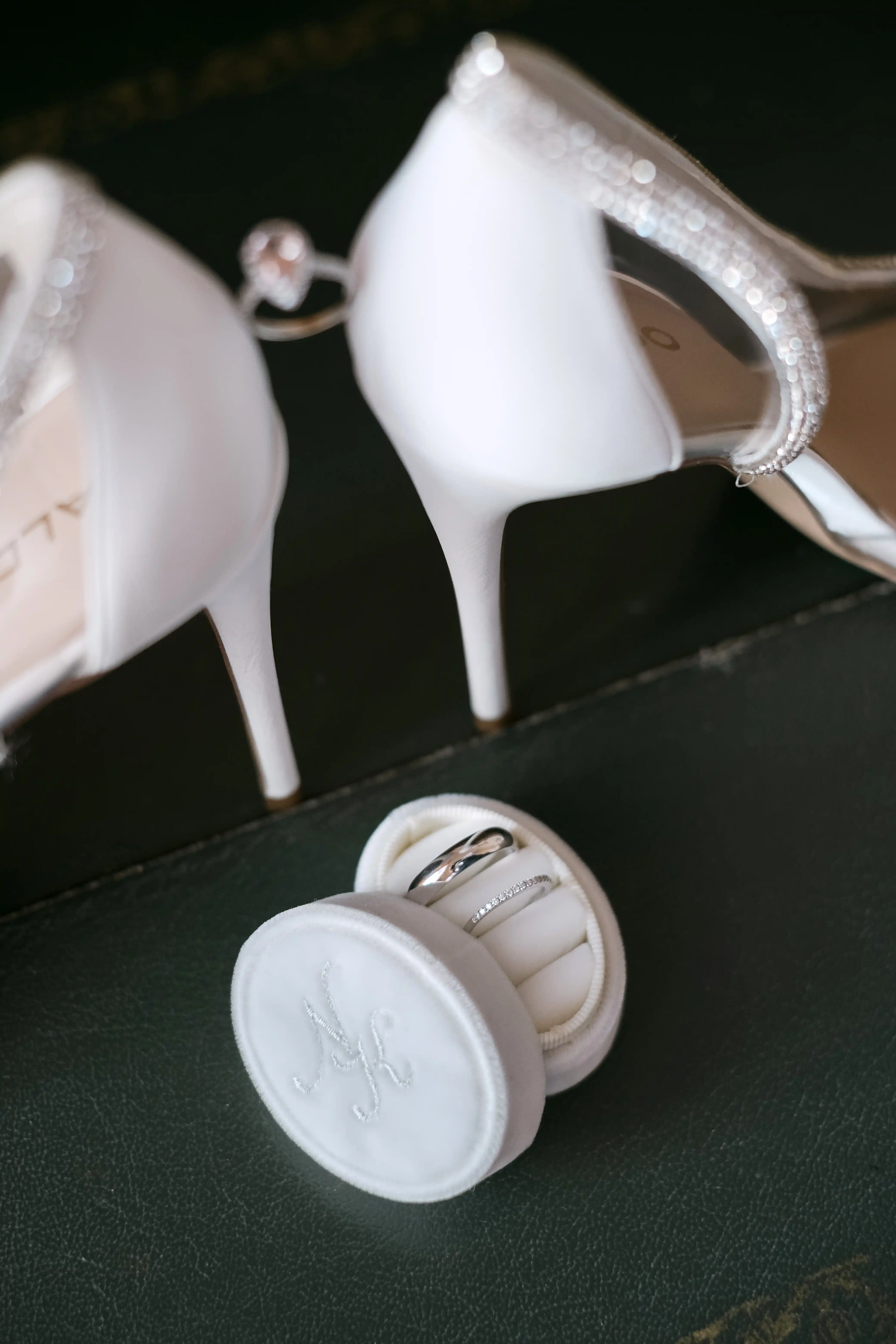 White bridal shoes with sparkling details next to wedding rings in an elegant box, luxury bridal preparation