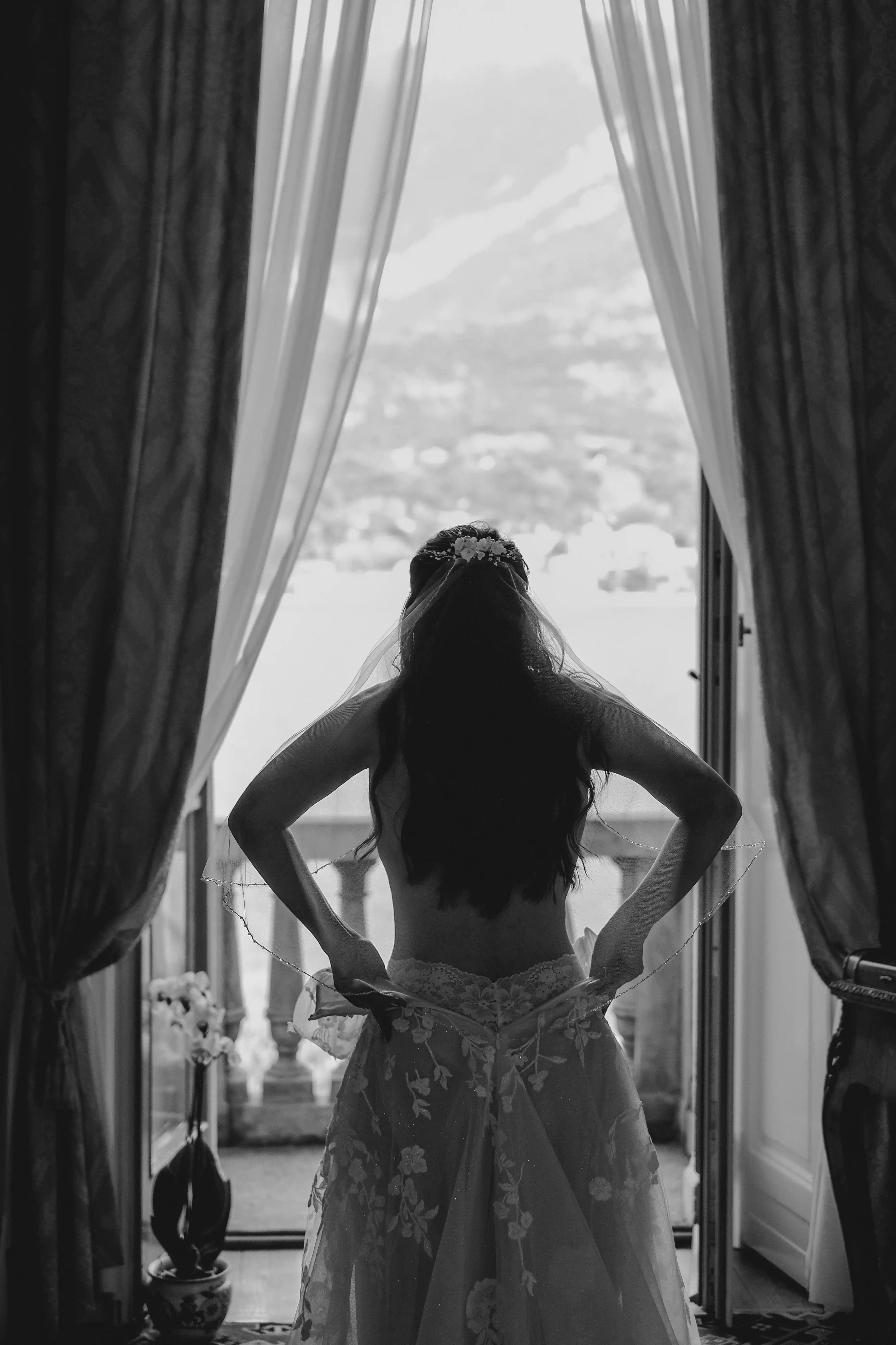 Bride standing by the window while getting dressed, natural light creating an elegant silhouette in a Lake Como villa