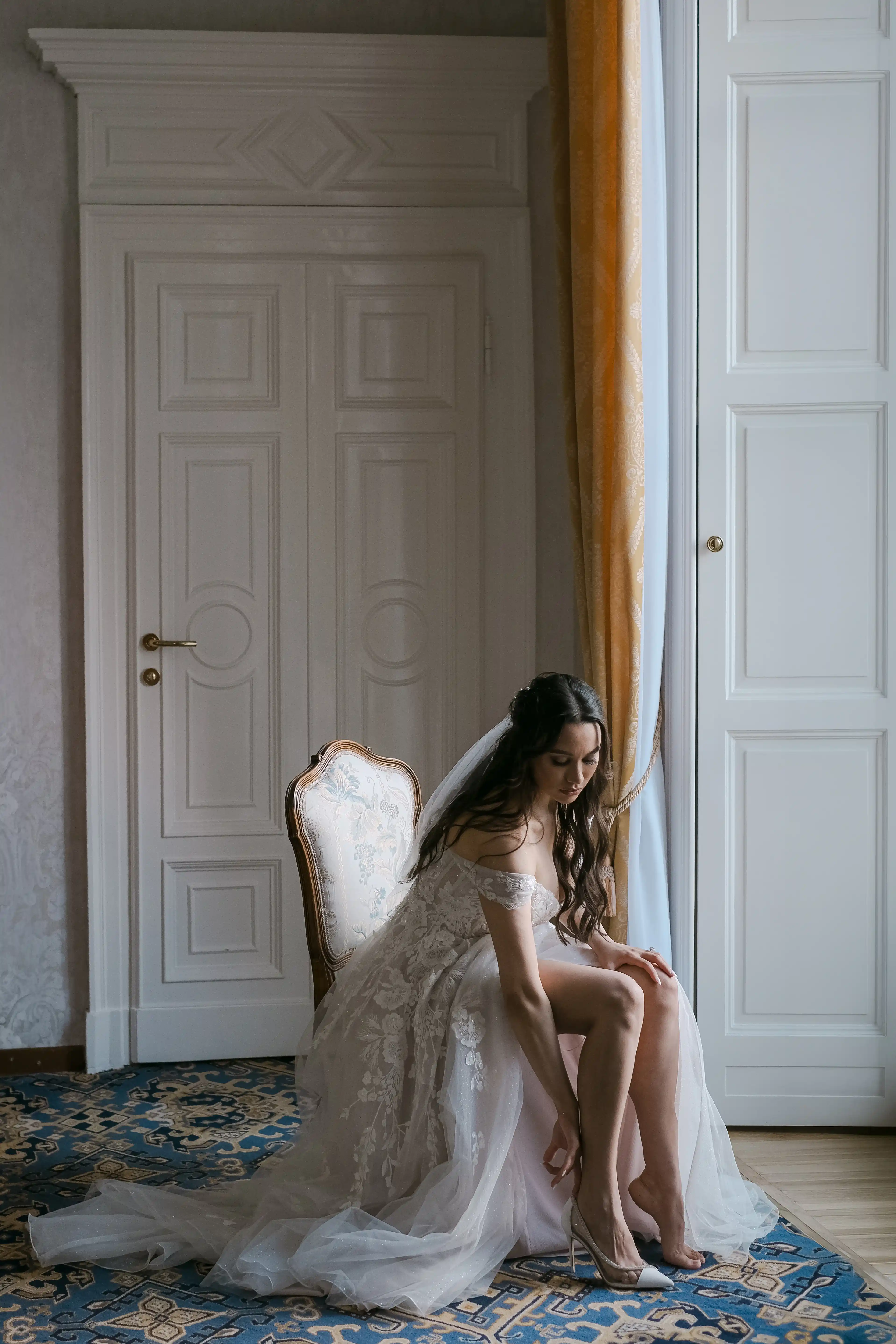 Bride sitting while putting on her shoes, soft light and refined atmosphere during bridal preparations