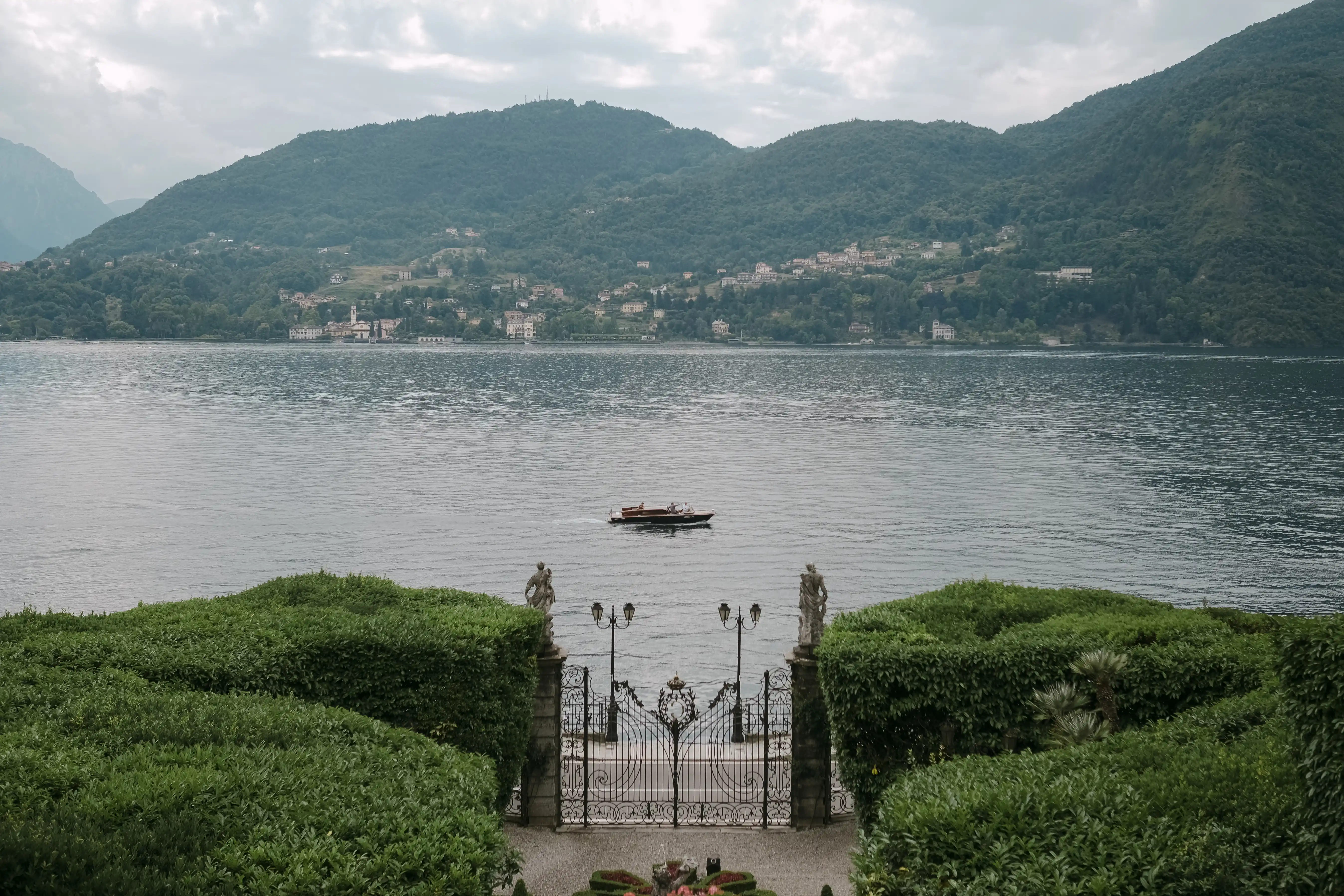 View of Lake Como from a villa garden with wrought iron gate and a boat crossing the water