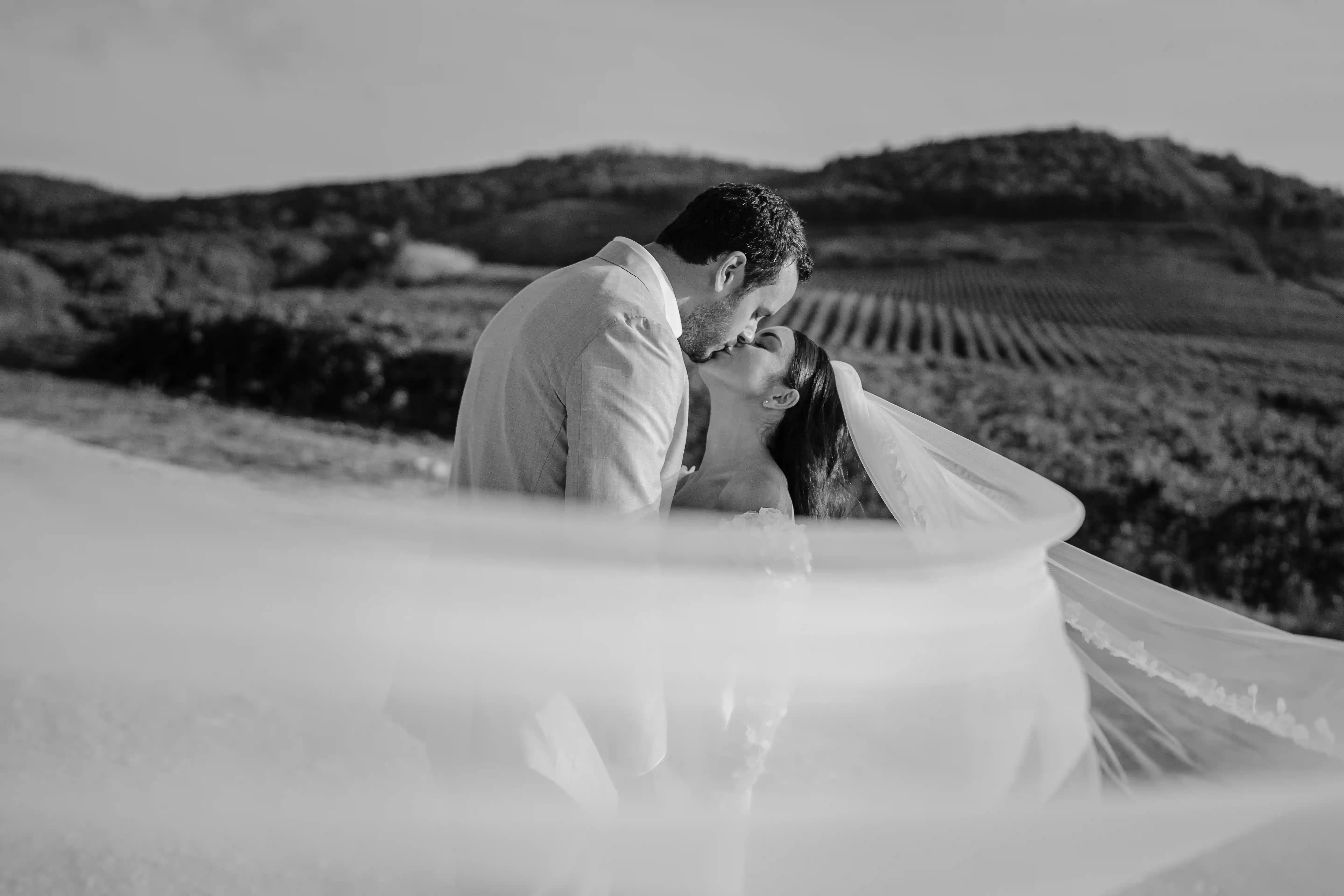 Black and white intimate kiss of bride and groom with flowing veil in rural Sicily