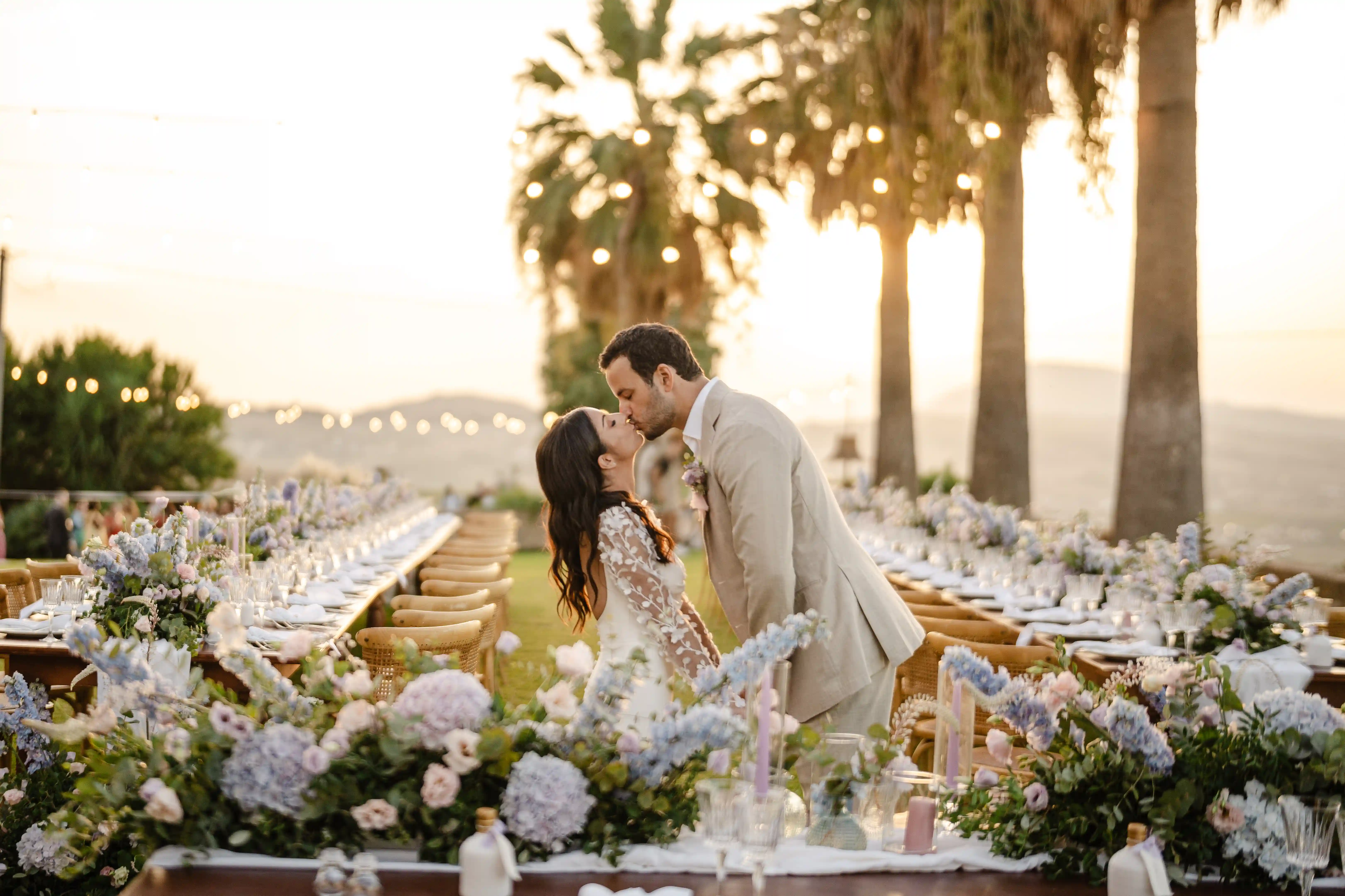 Bride and groom kissing between decorated reception tables at sunset wedding in Sicily