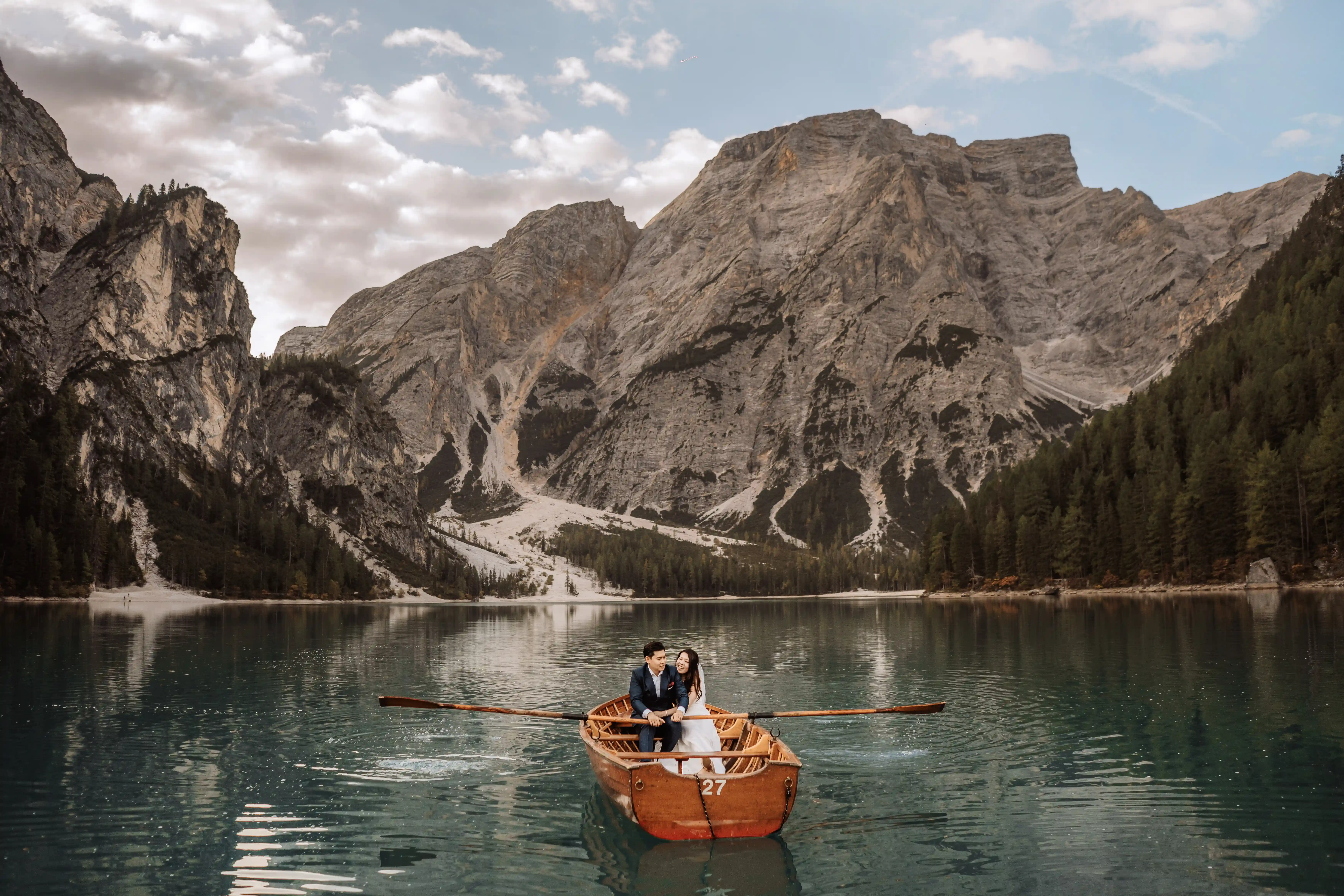 Couple sitting on a wooden boat in the middle of Lake Braies with panoramic Dolomites view