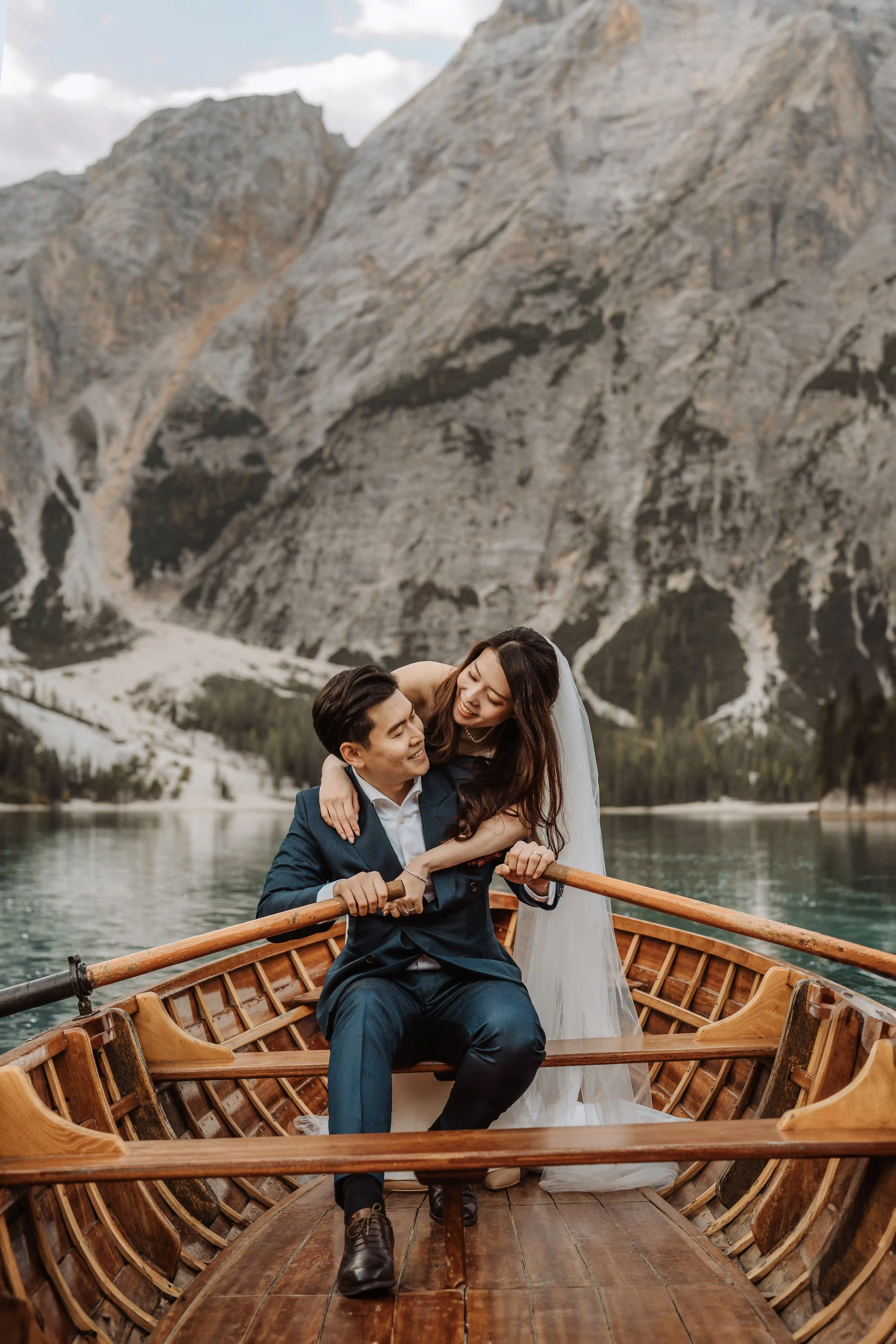 Groom rowing a wooden boat while bride hugs him during an intimate elopement at Lake Braies