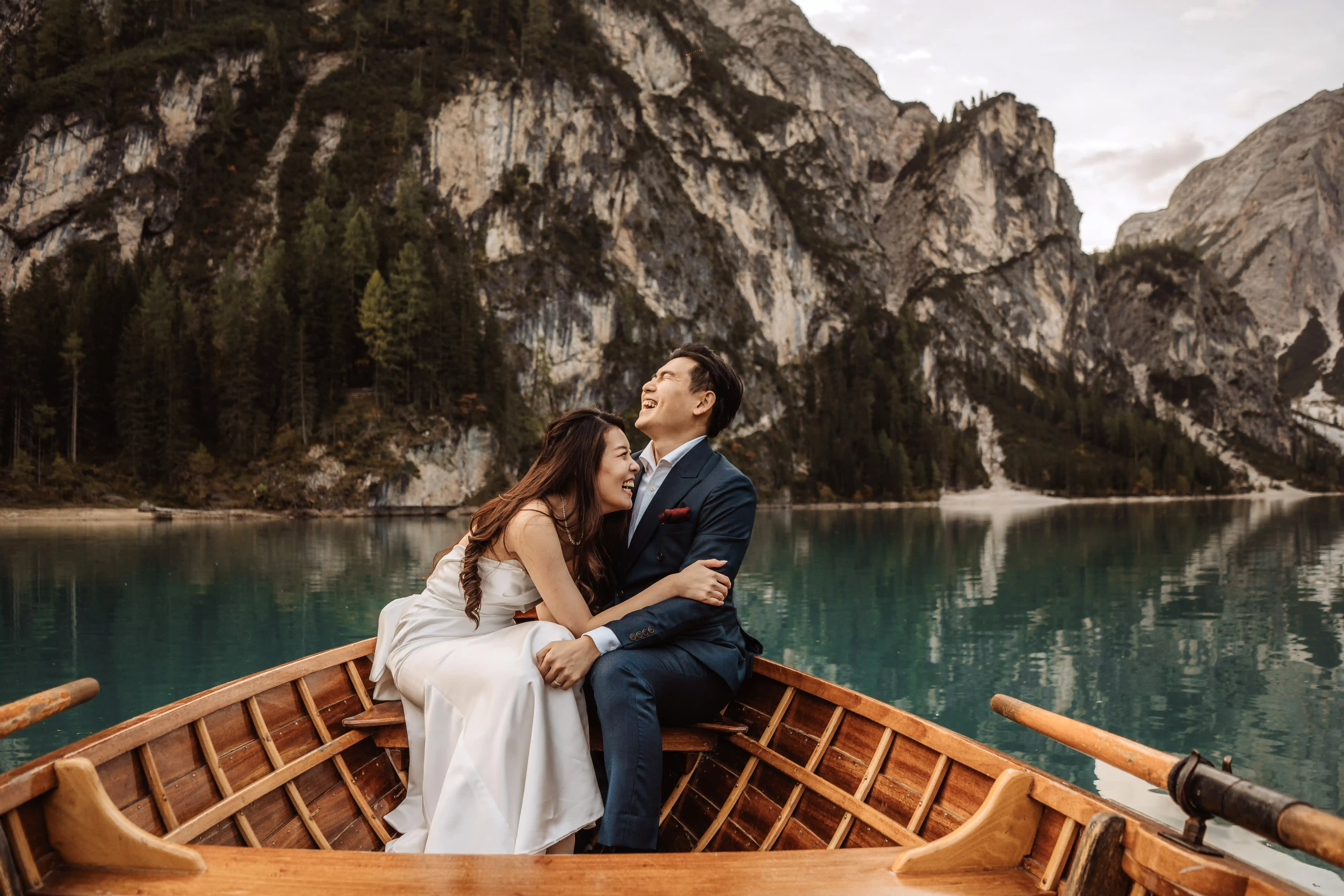 Joyful couple laughing together on a wooden boat during a Lake Braies elopement in the Dolomites