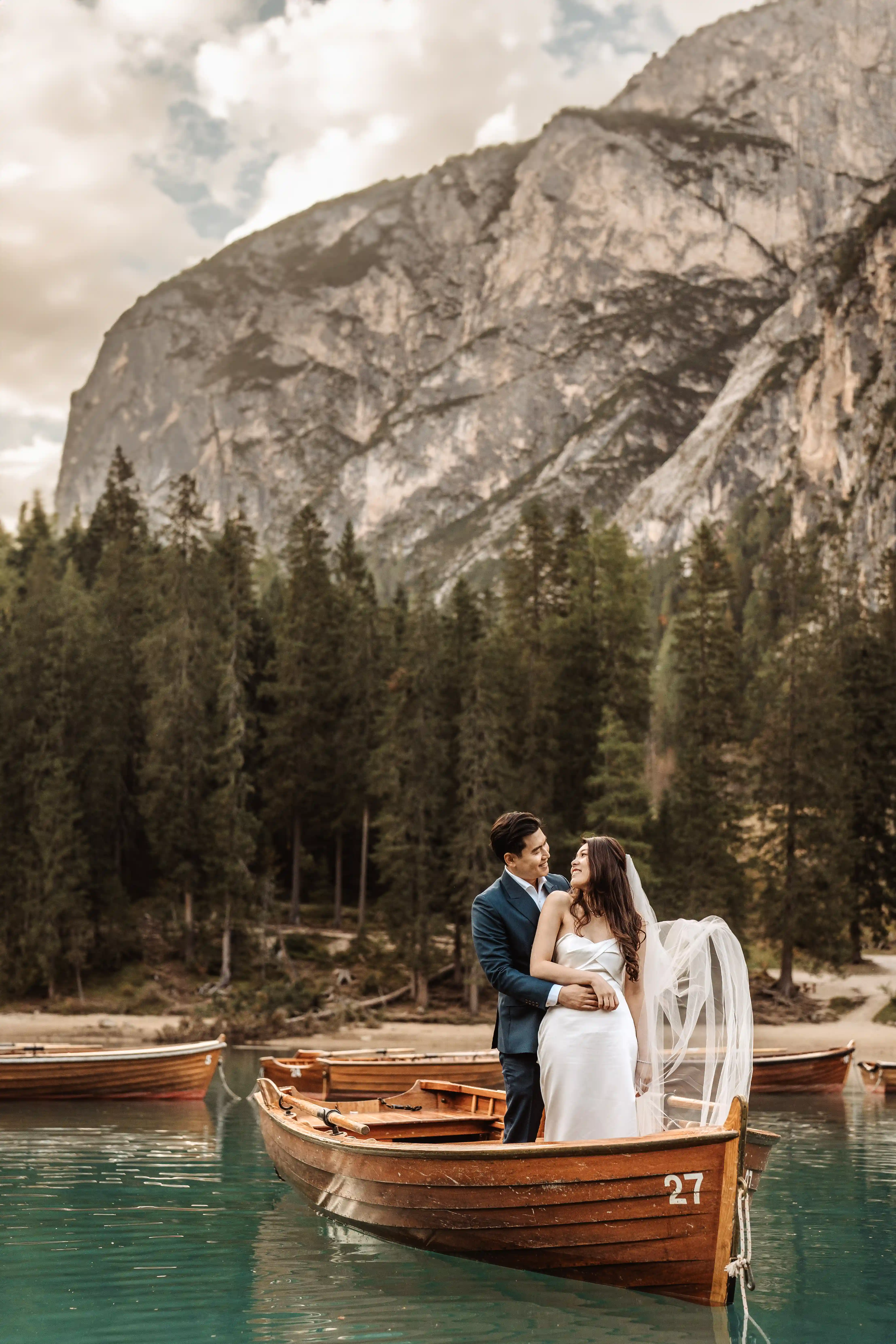 Bride and groom standing on a wooden boat at Lake Braies with dramatic Dolomites mountains behind