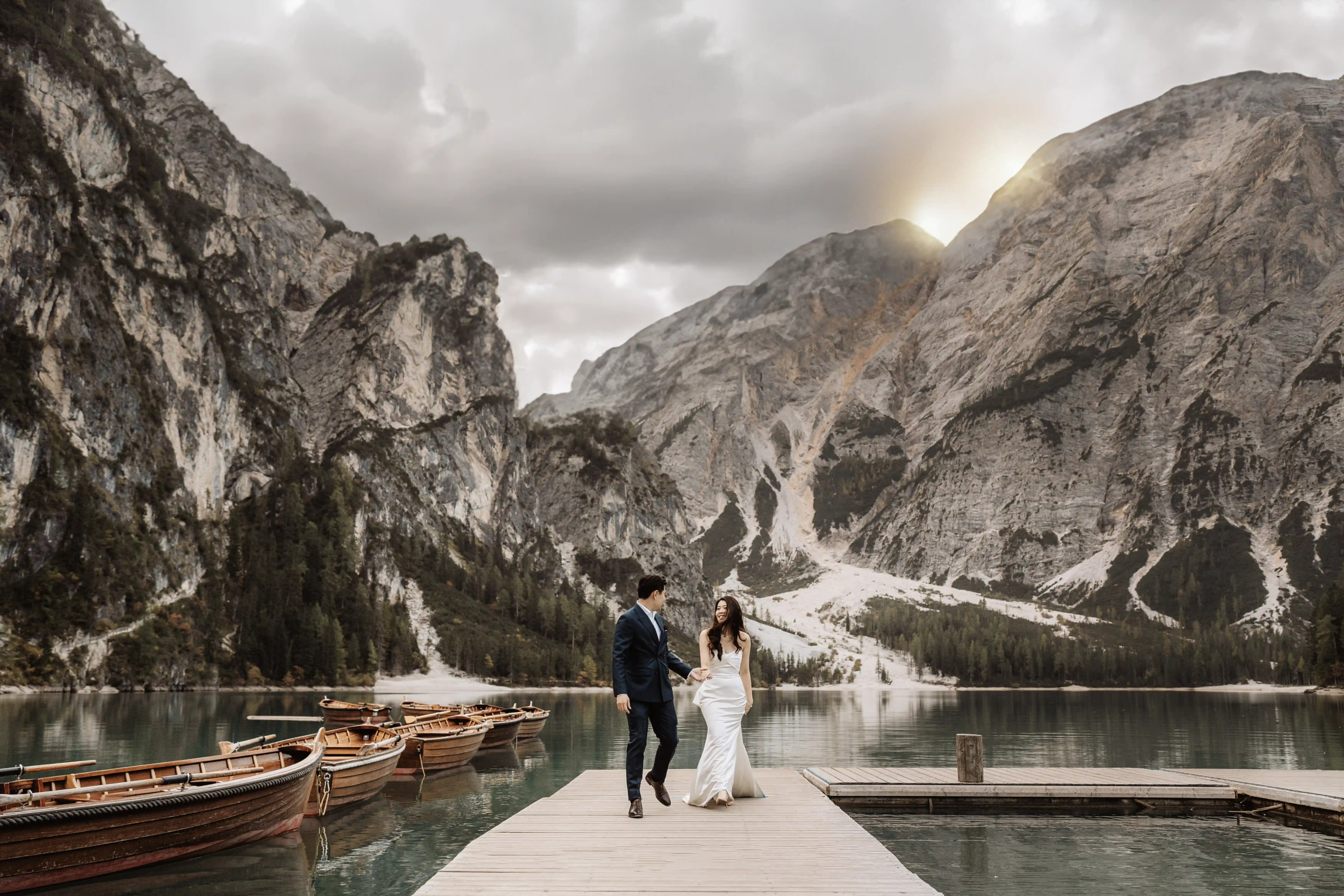 Bride and groom walking on a wooden pier at Lake Braies surrounded by mountains