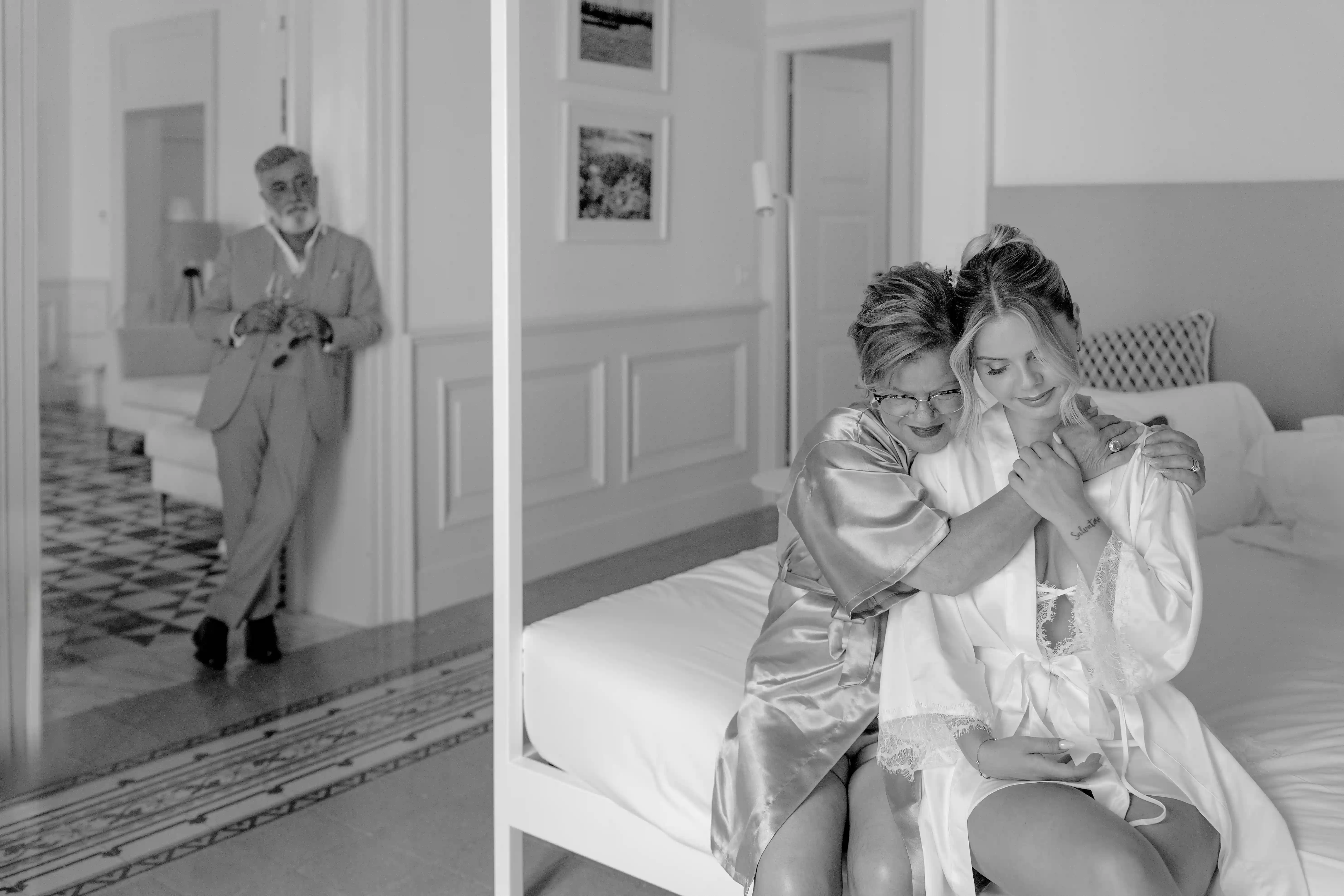 Black and white photo of the bride embraced by her mother with the father in the background