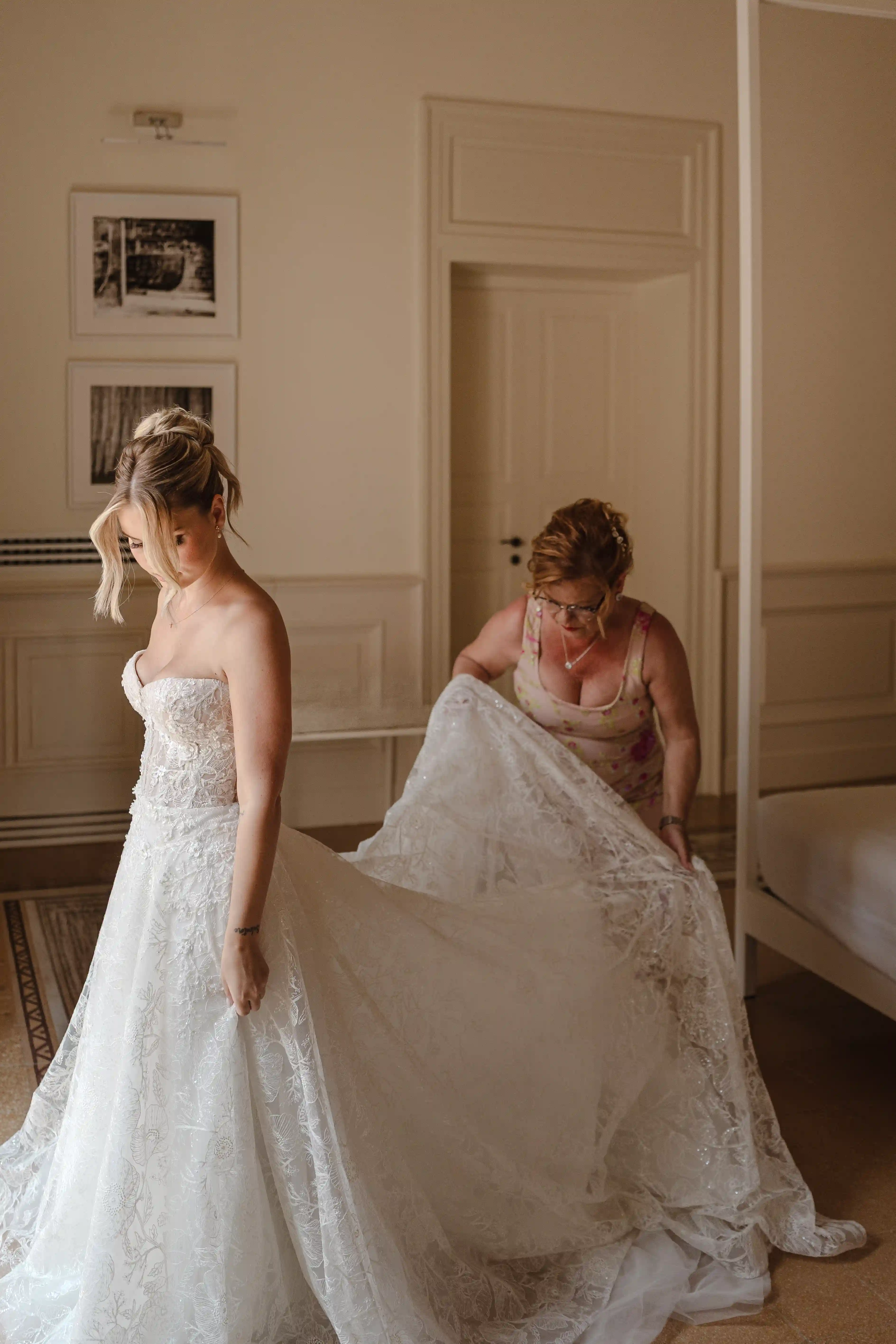 Bride getting dressed with her mother’s help in a softly lit room