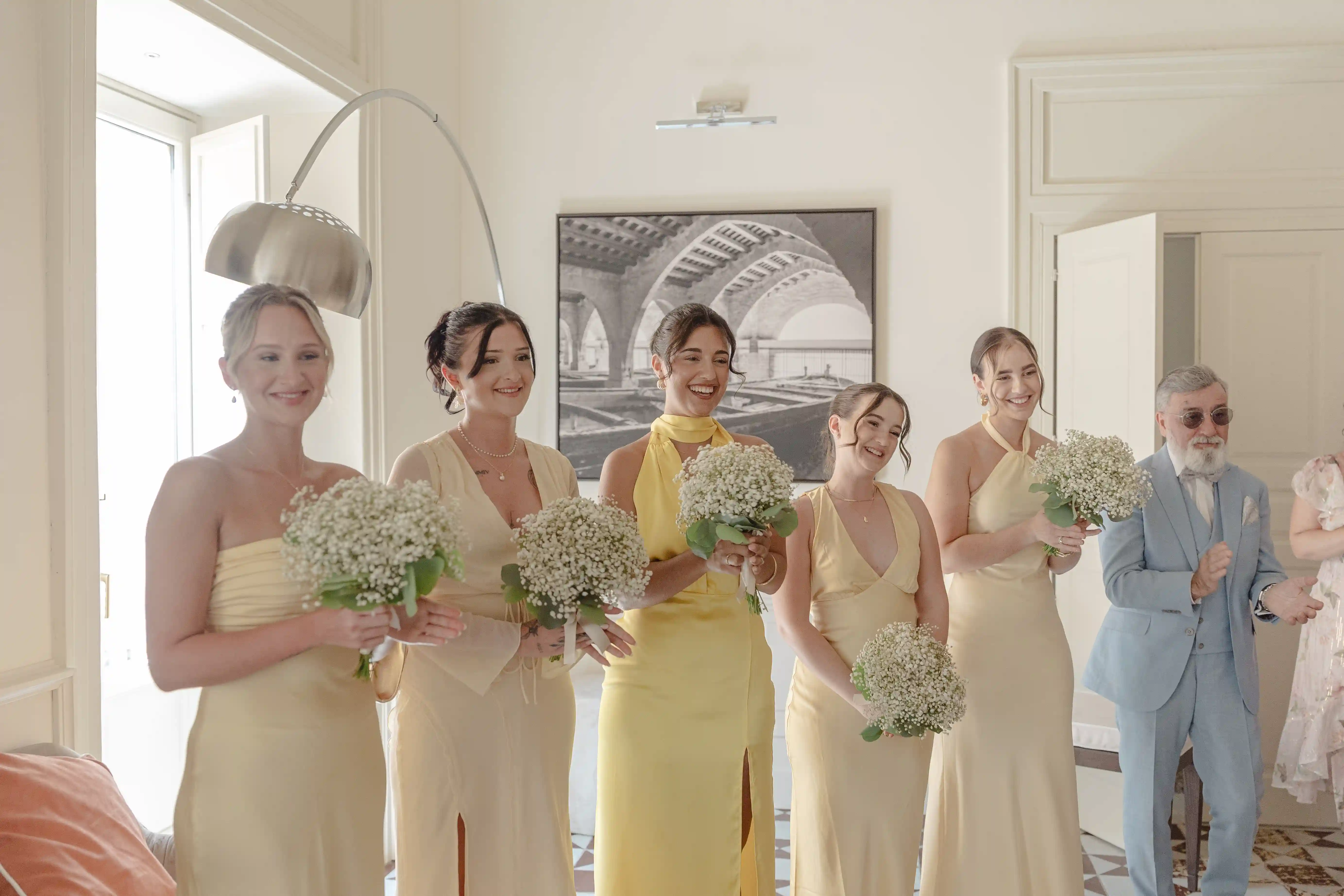 Bridesmaids in yellow dresses holding white flower bouquets during wedding preparations