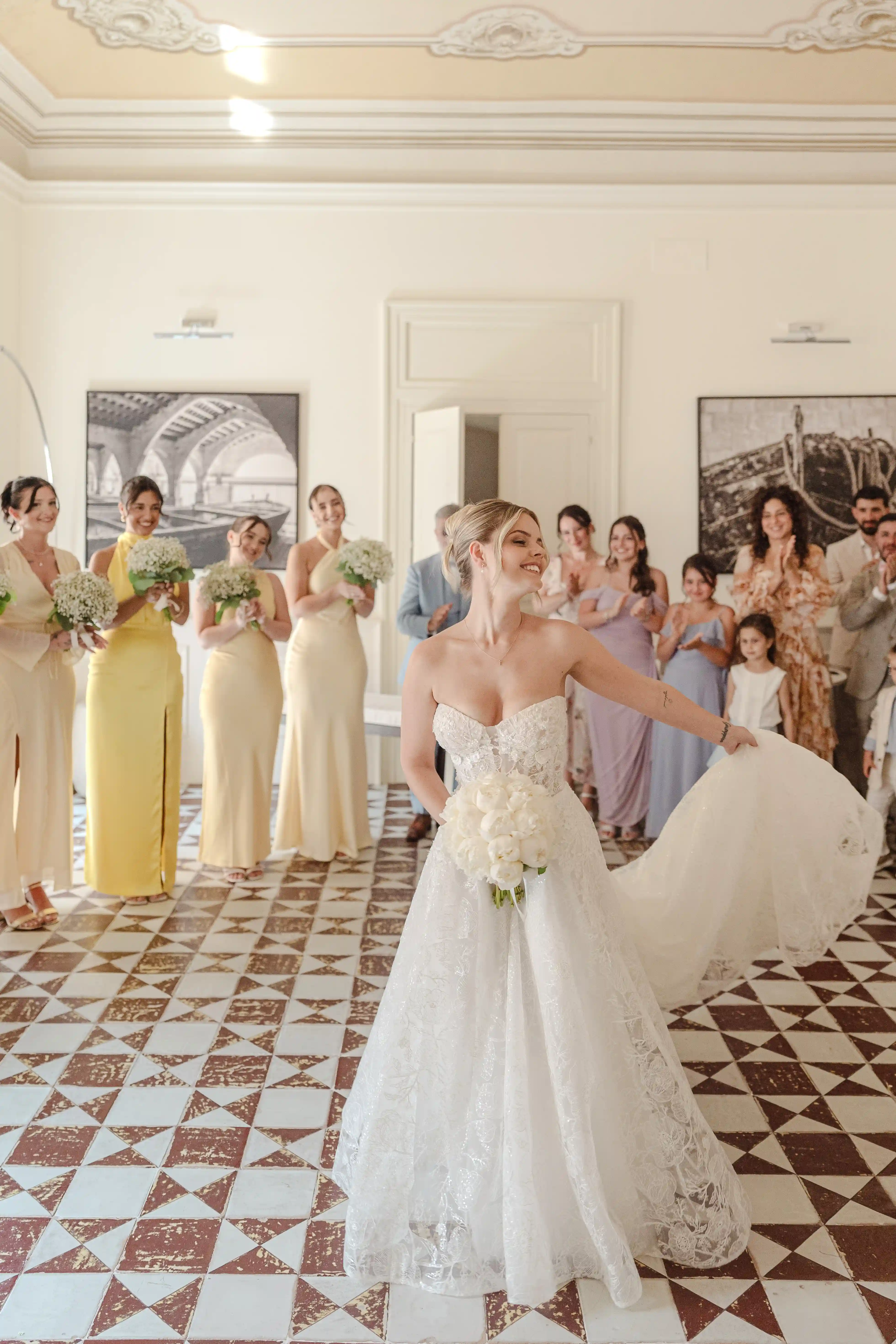 Bride twirling in her lace wedding dress while bridesmaids in yellow dresses smile in an elegant Sicilian villa