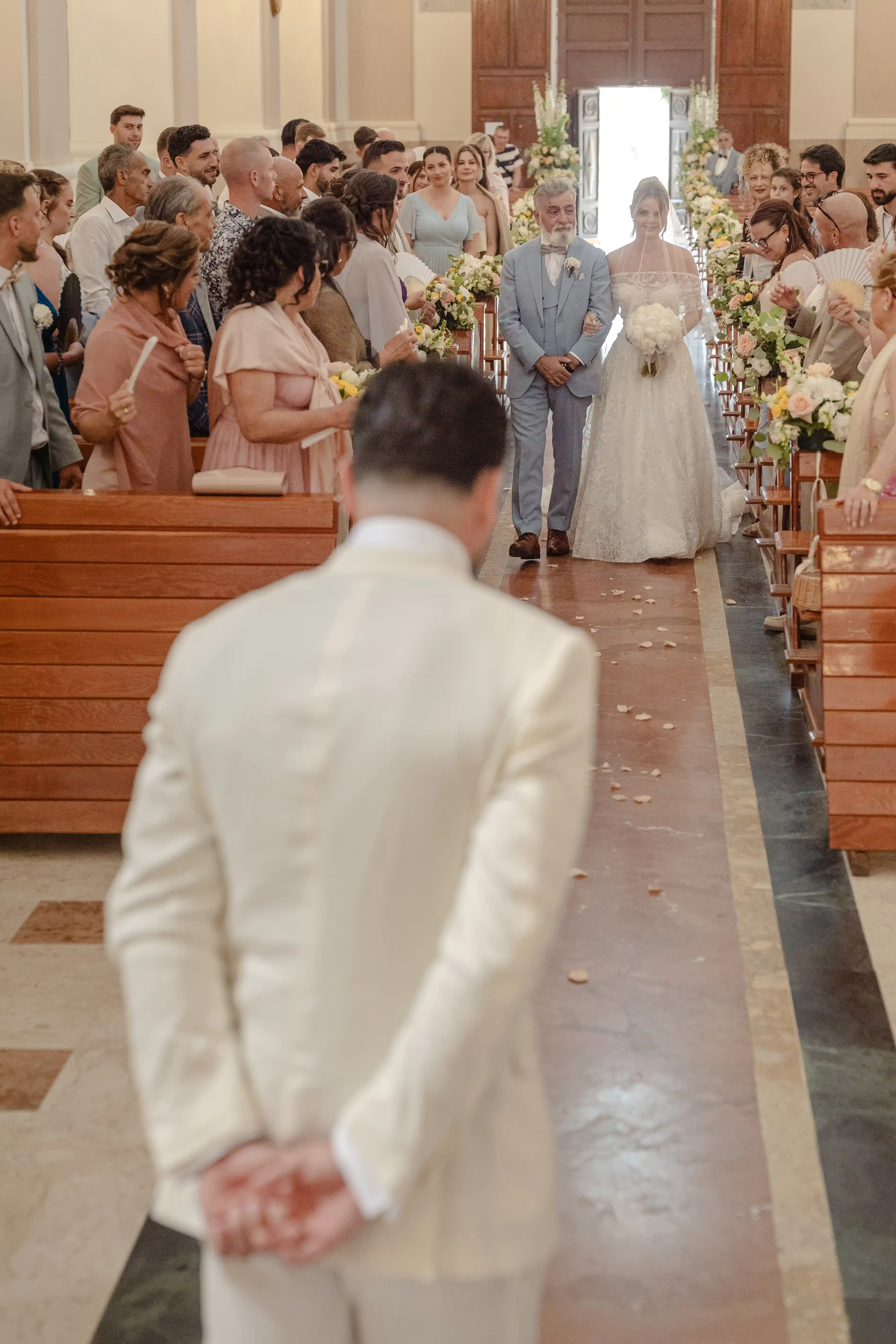 Bride entering the church with her father as guests watch and petals line the aisle