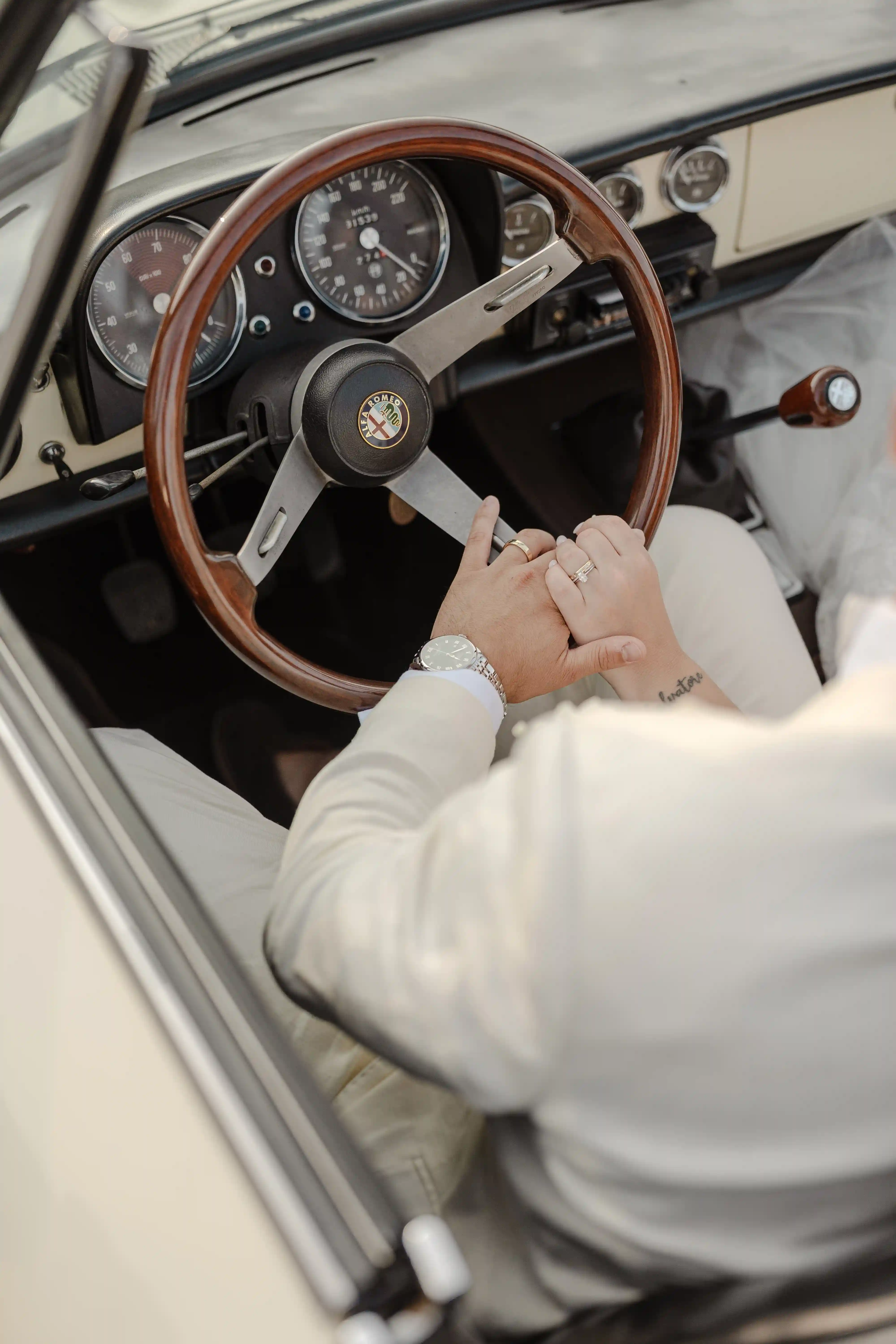 Bride and groom holding hands on vintage Alfa Romeo steering wheel