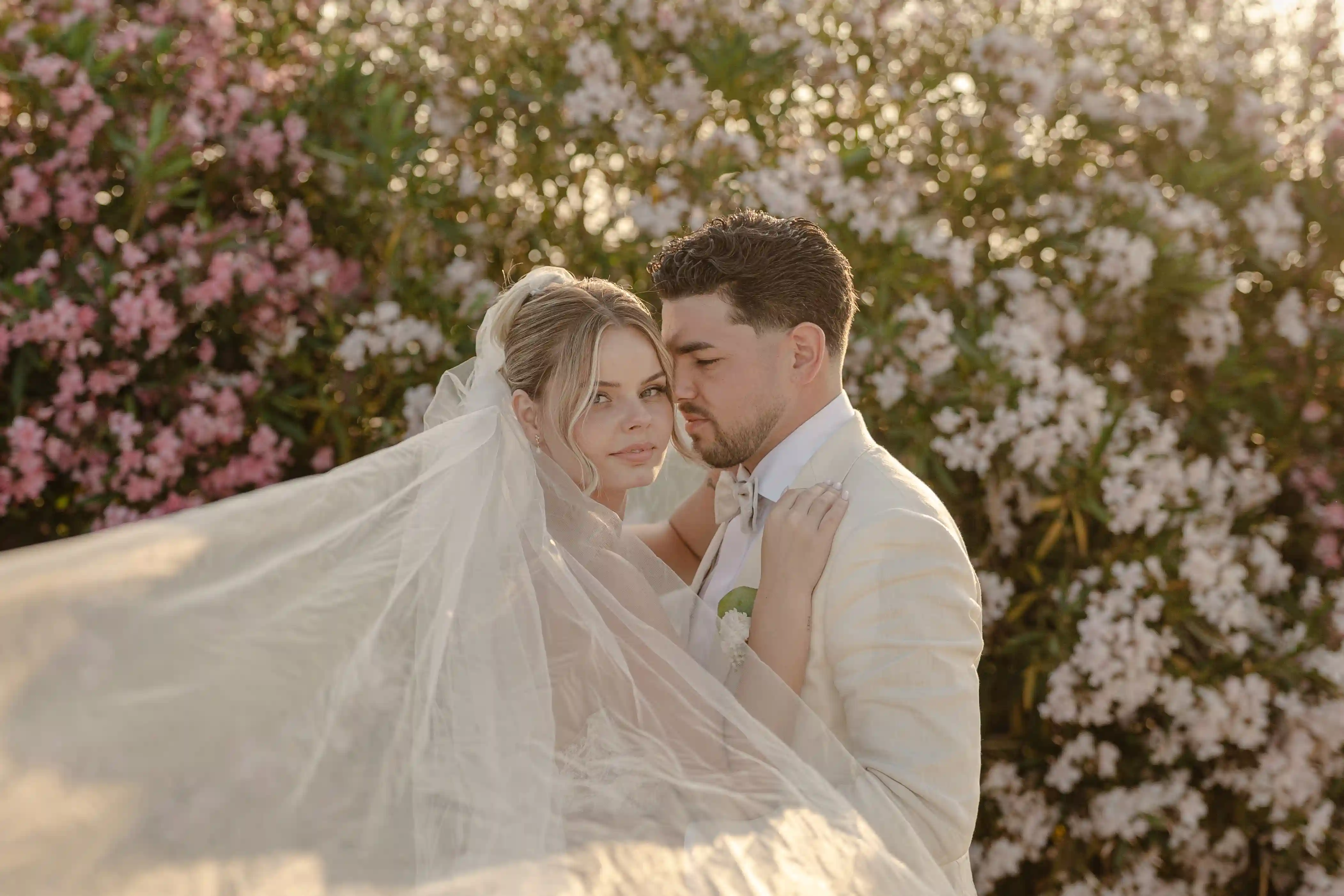Romantic portrait of bride and groom with flowing veil and floral background