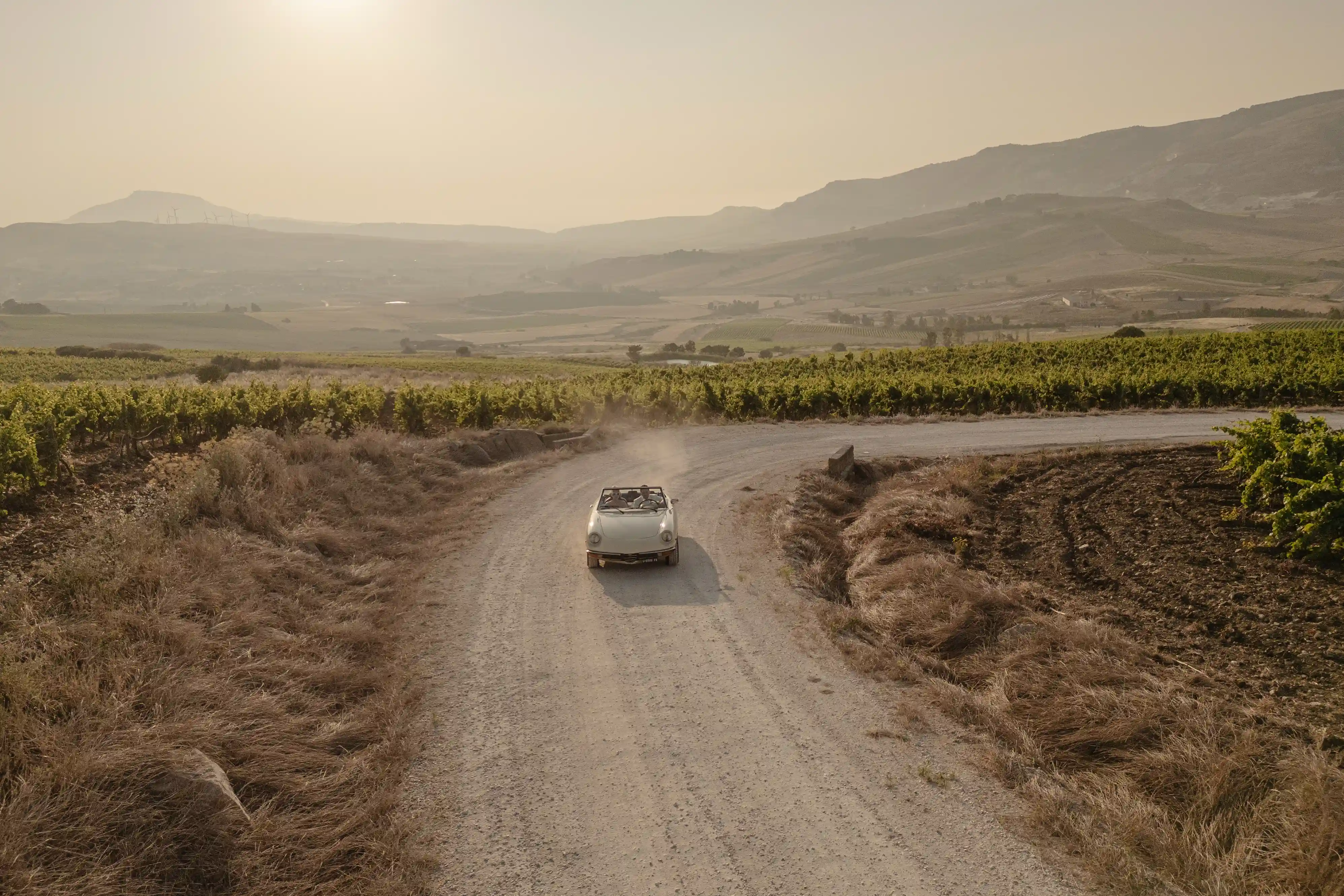 Vintage wedding car driving along dusty road through Sicilian landscape