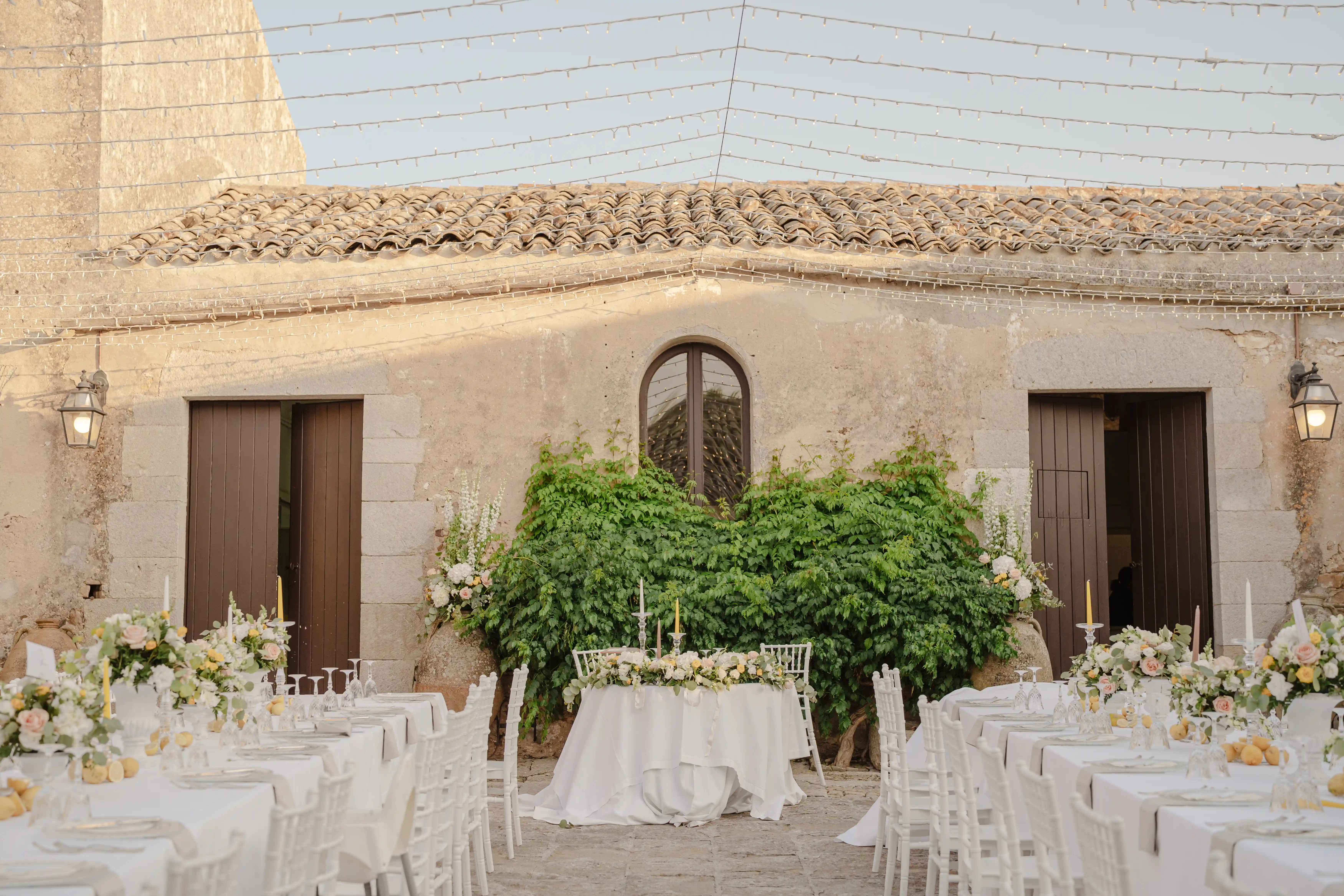 Elegant outdoor wedding reception setup with floral decorations in rustic Sicilian courtyard
