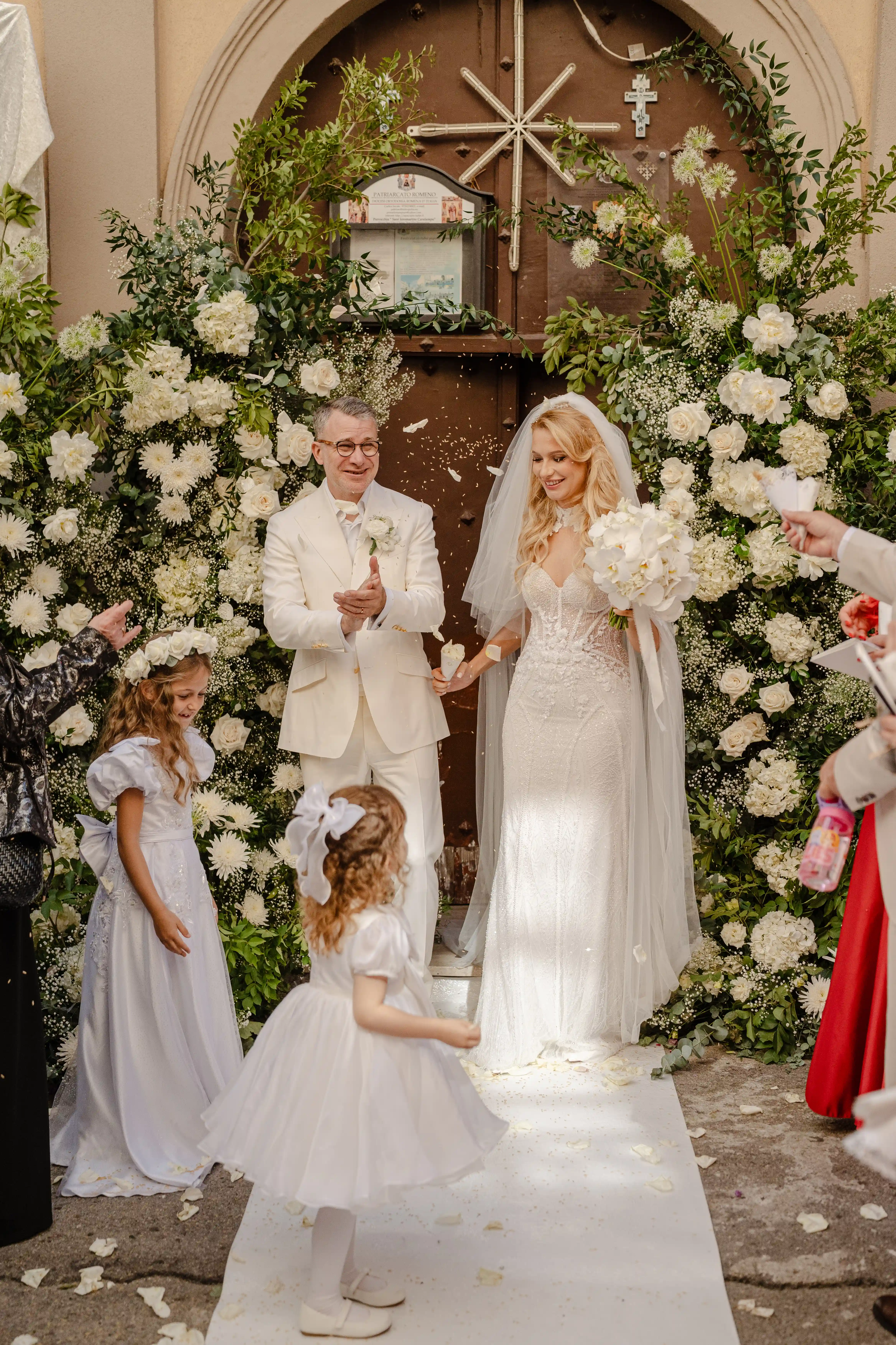 Newlyweds walking out of the ceremony surrounded by white flowers and petals at Tenuta Calamuletti Sicily