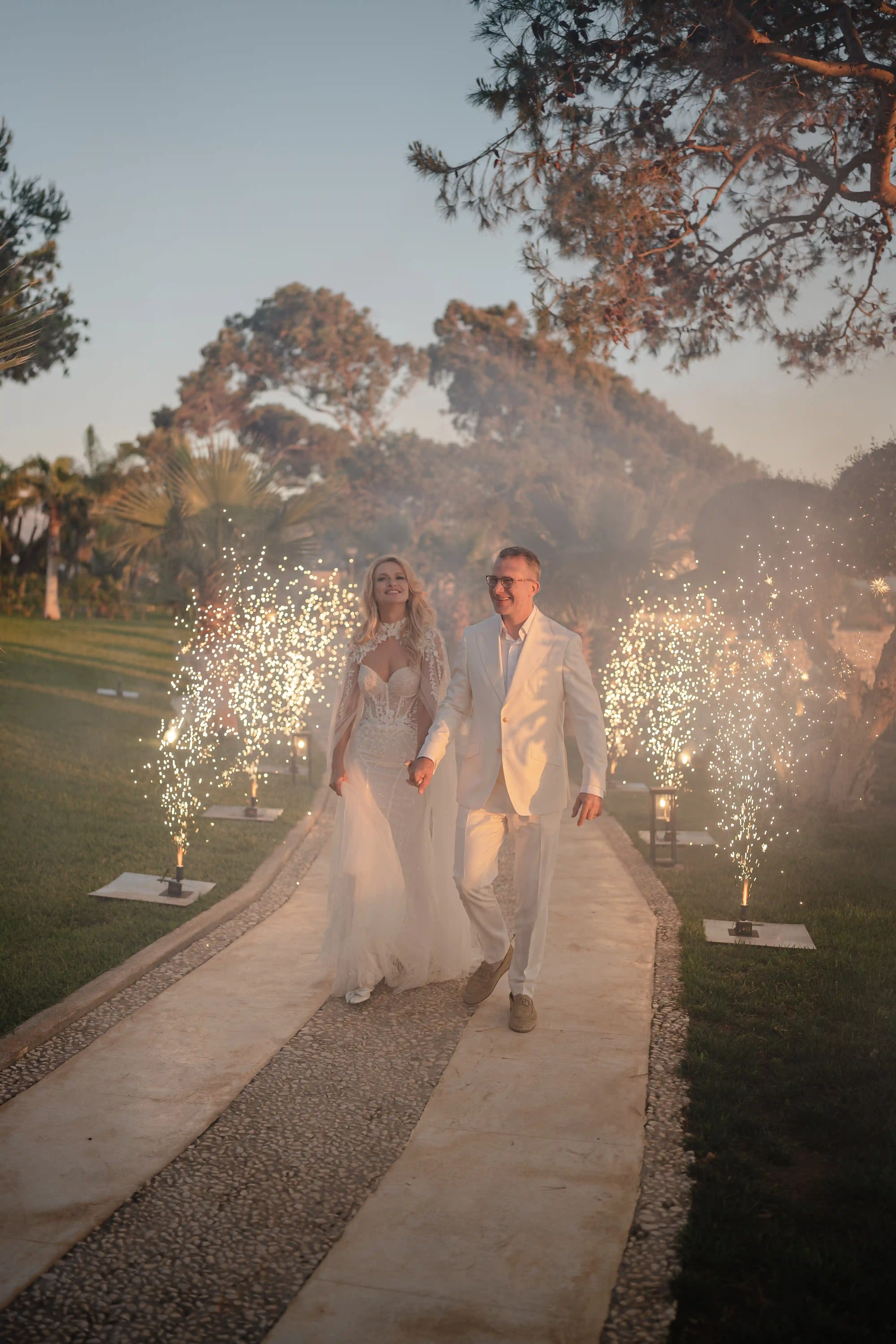 Bride and groom walking through sparkling lights during evening wedding celebration in Sicily