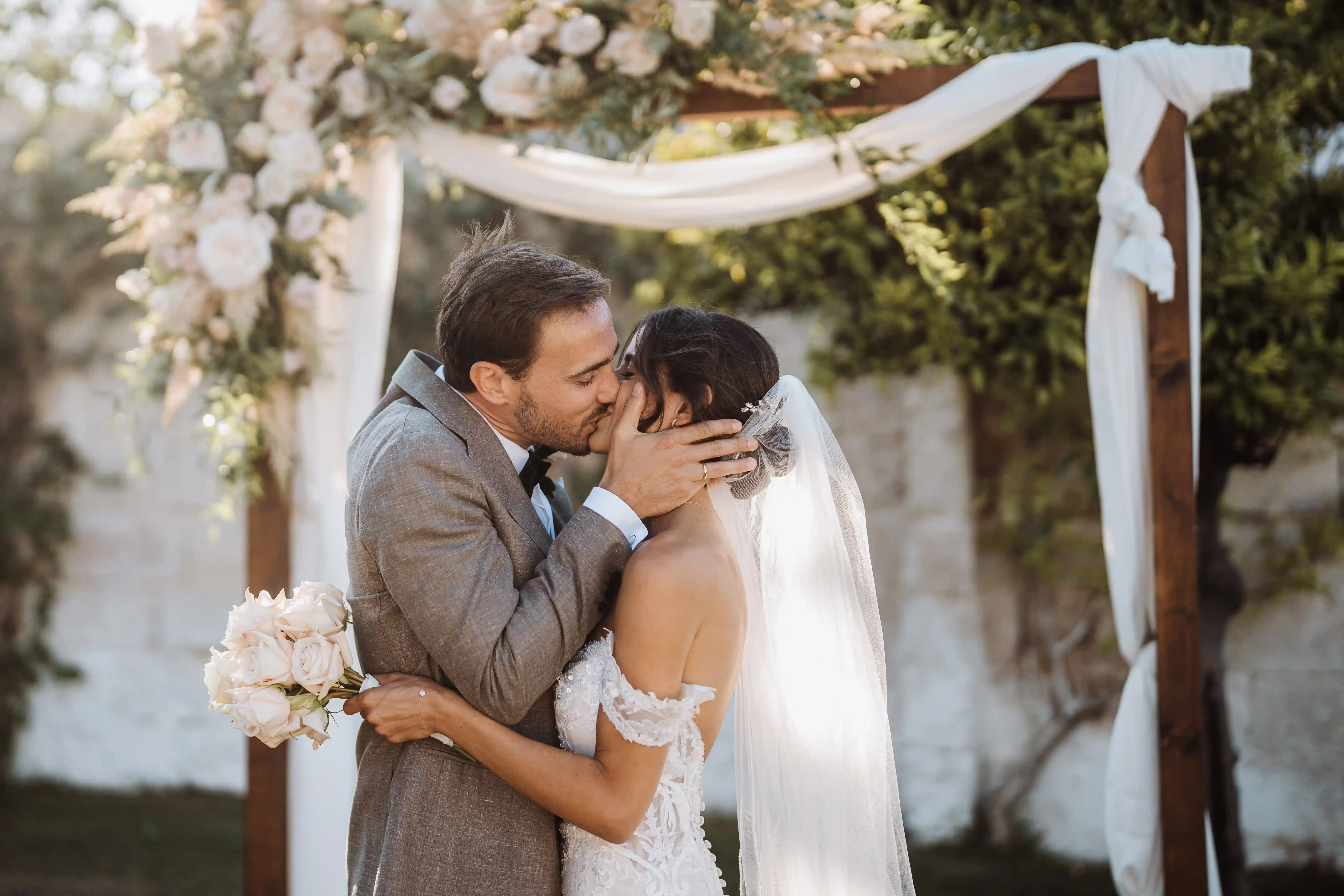 Romantic outdoor wedding ceremony kiss in Puglia under floral arch, Italian countryside masseria wedding