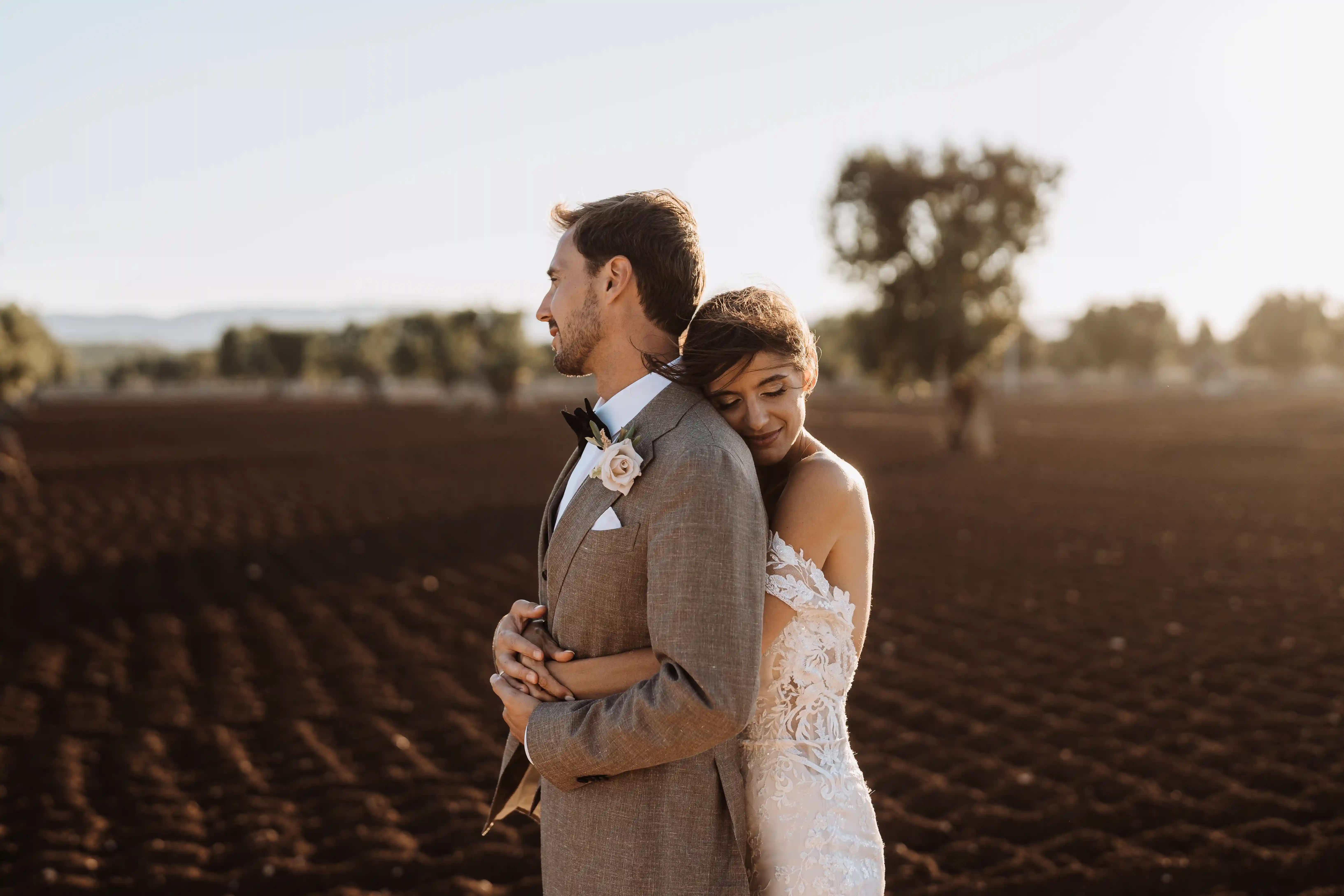Bride and groom embracing in sunlit field in Apulia, natural and emotional destination wedding in Italy