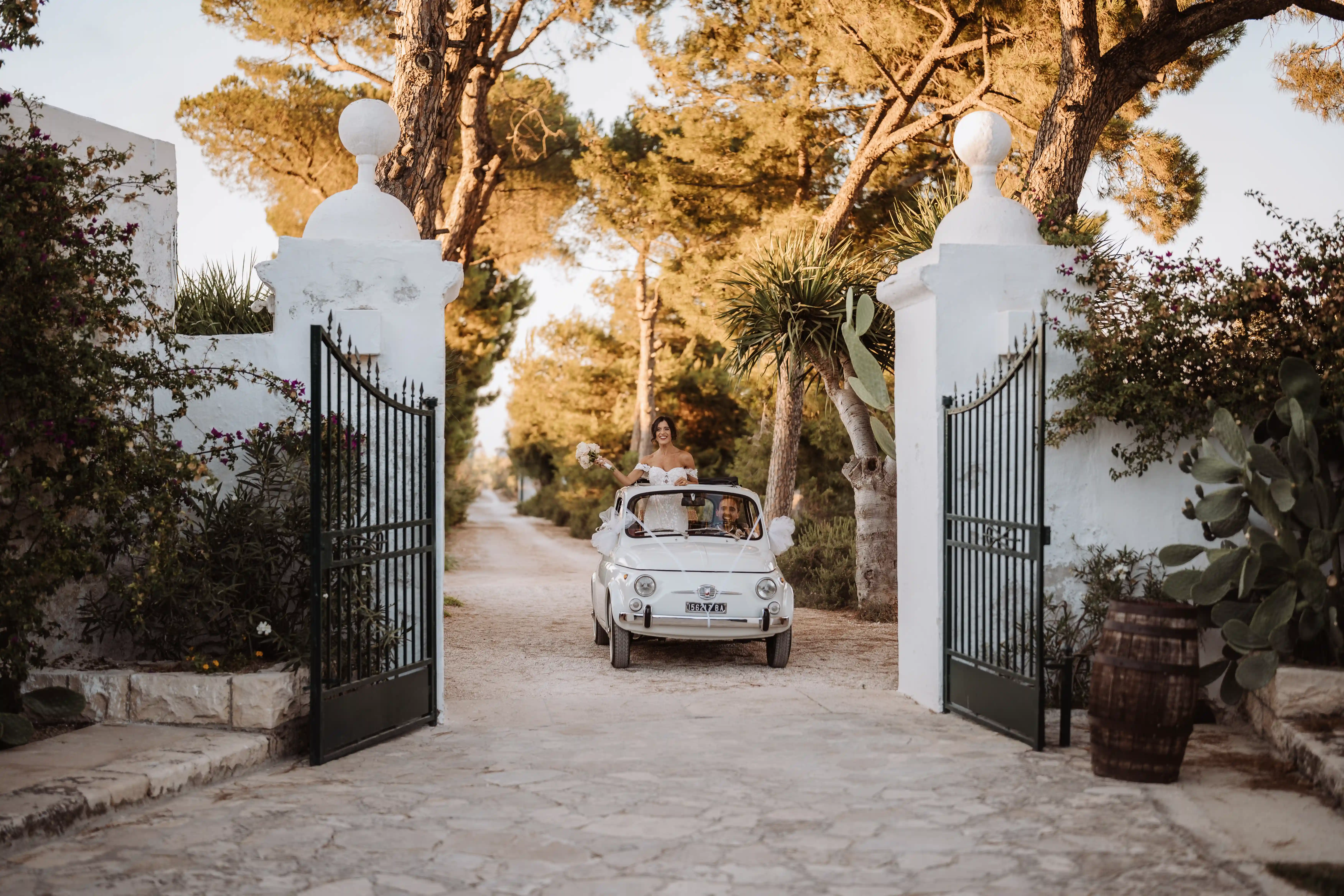 Bride arriving in vintage Fiat 500 at a Puglia masseria entrance at sunset
