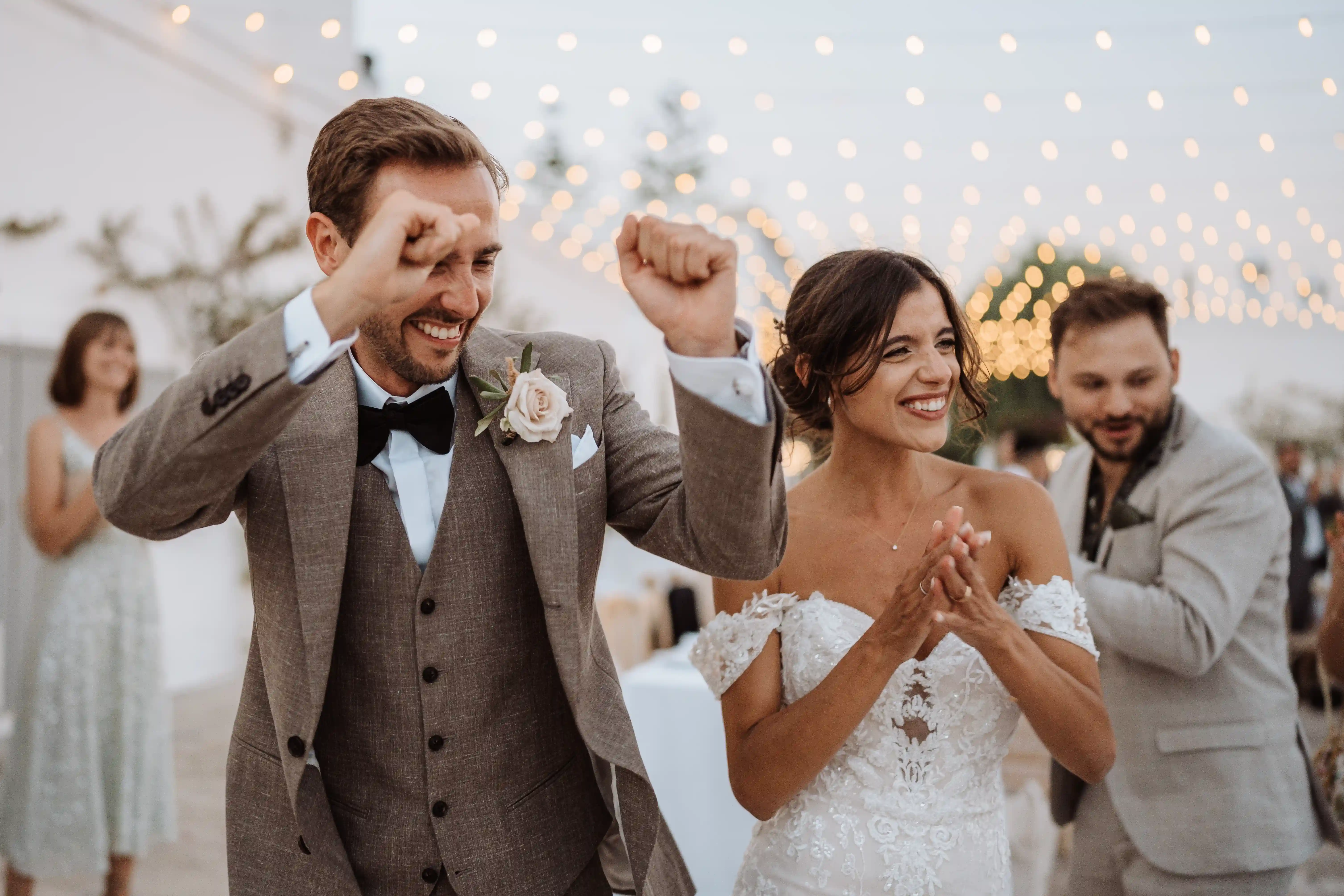 Newlyweds celebrating joyfully under string lights during evening wedding party
