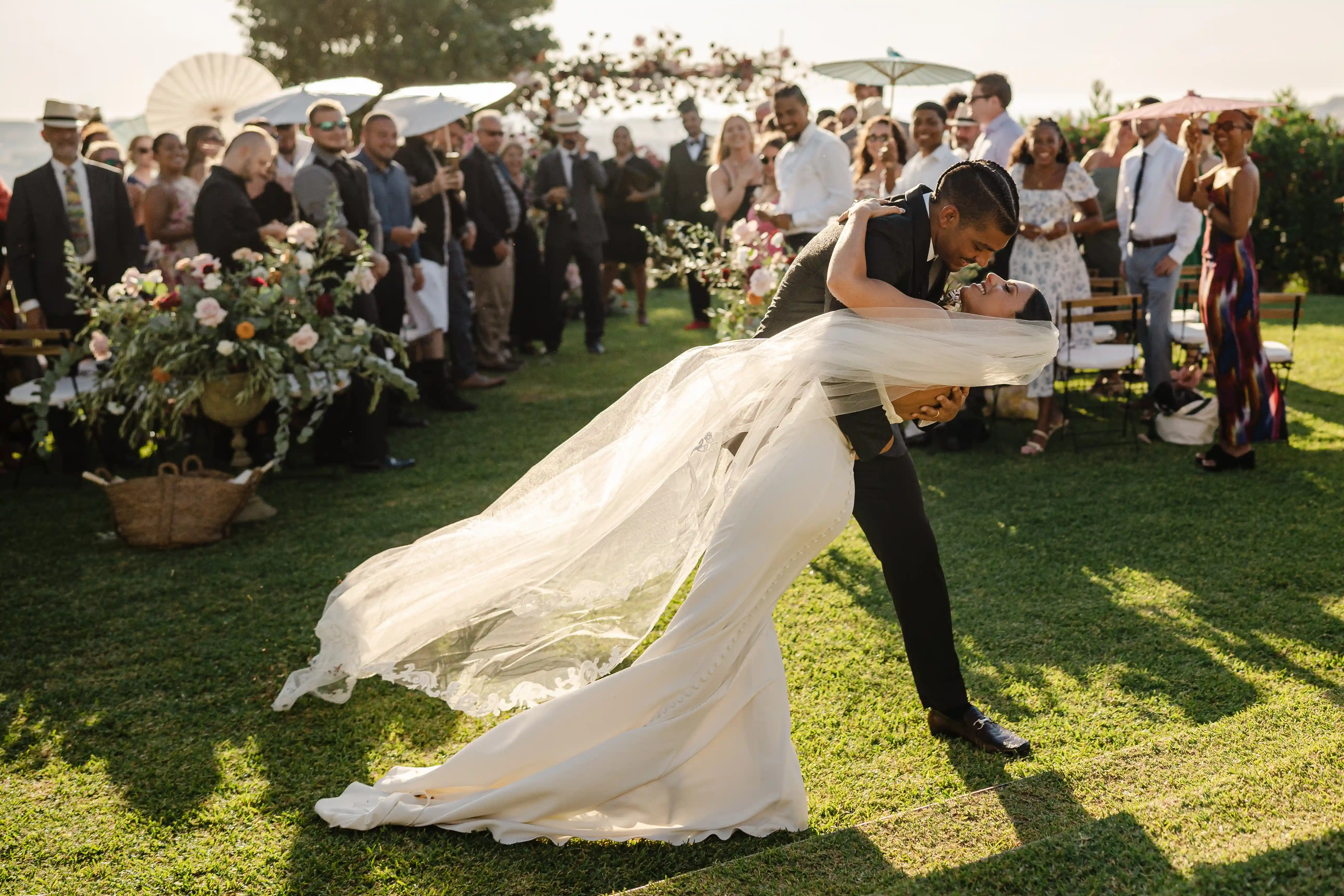 Groom holding the bride in a deep dip as her veil flows in the air, sharing a kiss during the ceremony while guests smile and watch in the background.