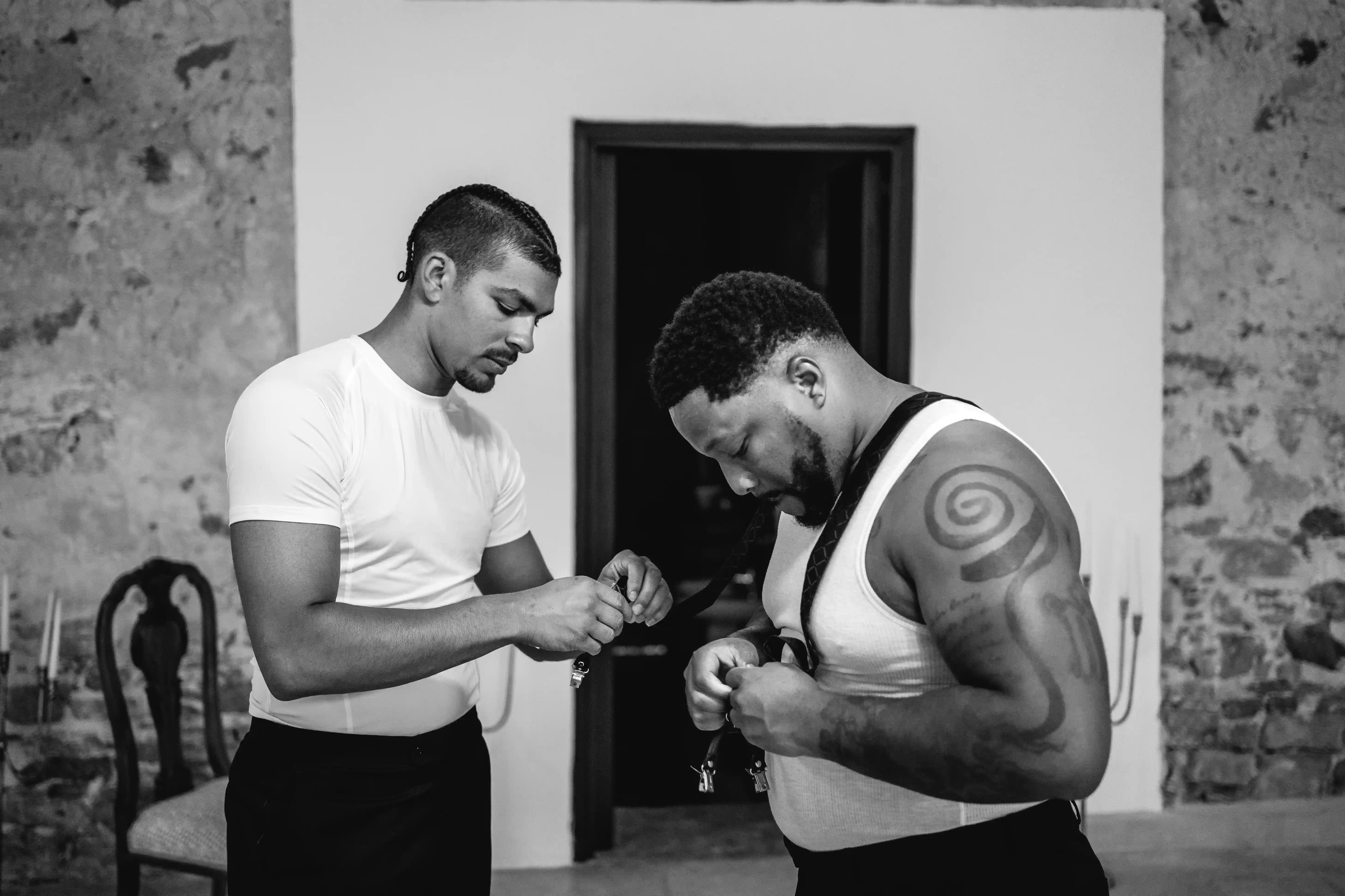 Groom being helped into his outfit during relaxed and intimate wedding preparations.